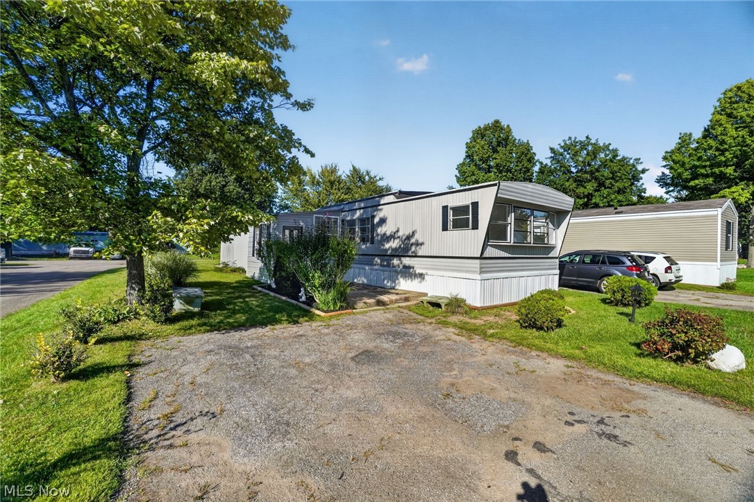 Manufactured home with a projecting front window beside a gravel driveway and parked cars.