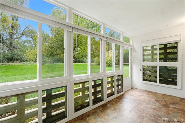 Bright sunroom with expansive windows overlooking a green lawn and mature trees.