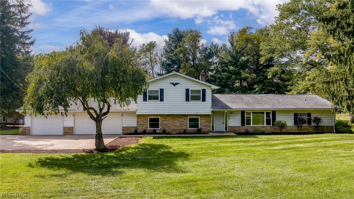 Split-level house with a three-car garage, brick accents, and a mature tree shading the front lawn.