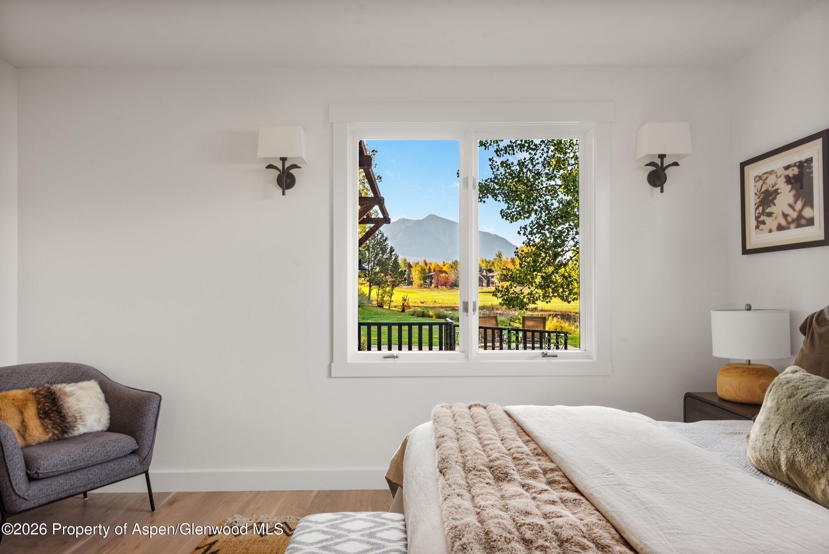 Bedroom with a mountain view through the window, a white bed, and a gray reading chair.