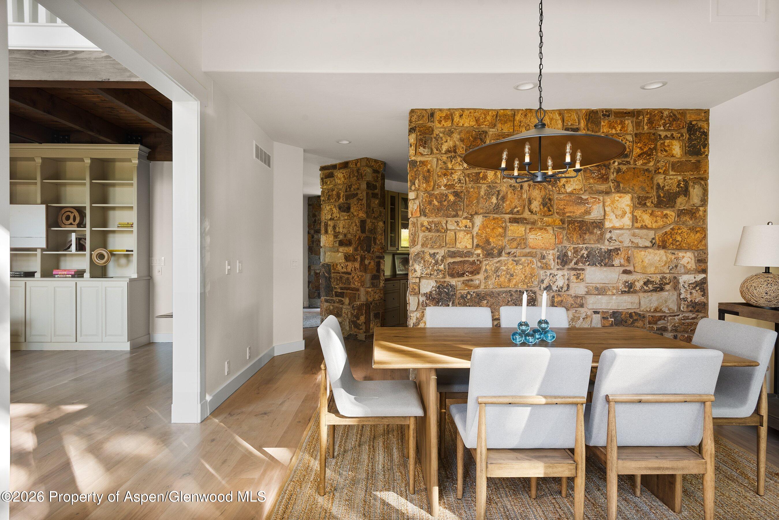 Dining room with a large stone accent wall, wood table, and upholstered chairs.
