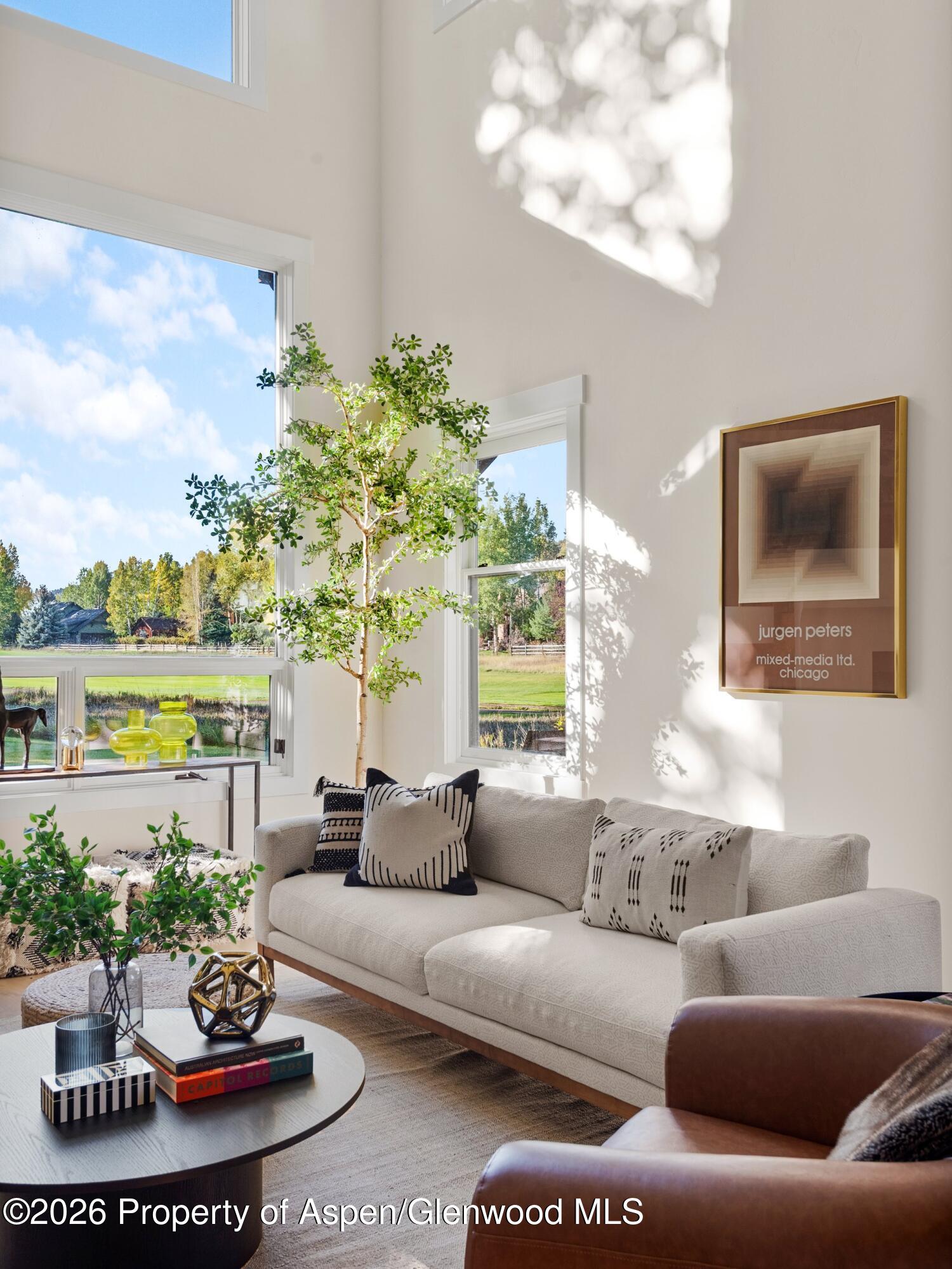 Bright living room with tall windows, a neutral sofa, and sunlight filtering across the walls.