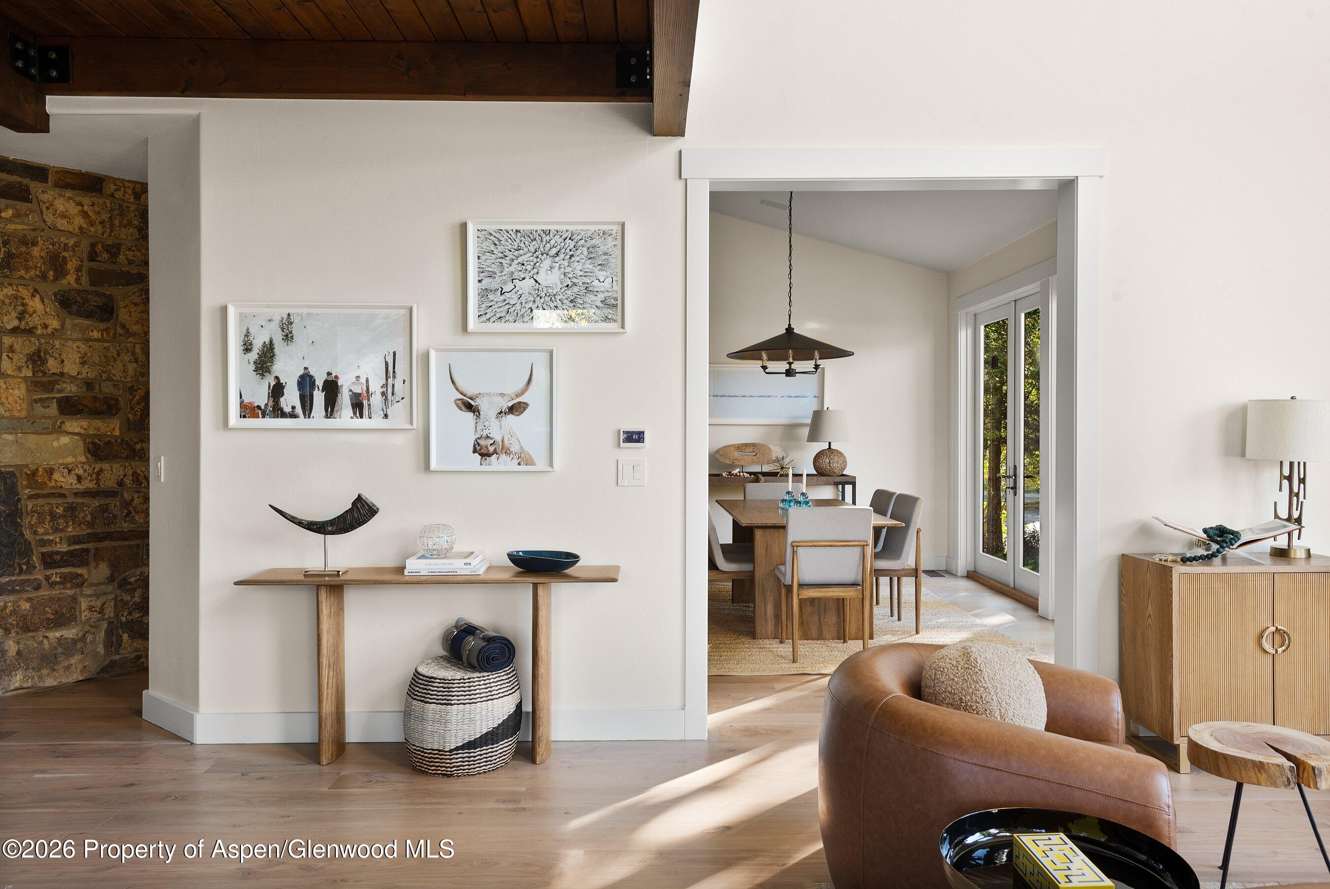 Open living area with exposed timber beams, stone fireplace, and dining room beyond.