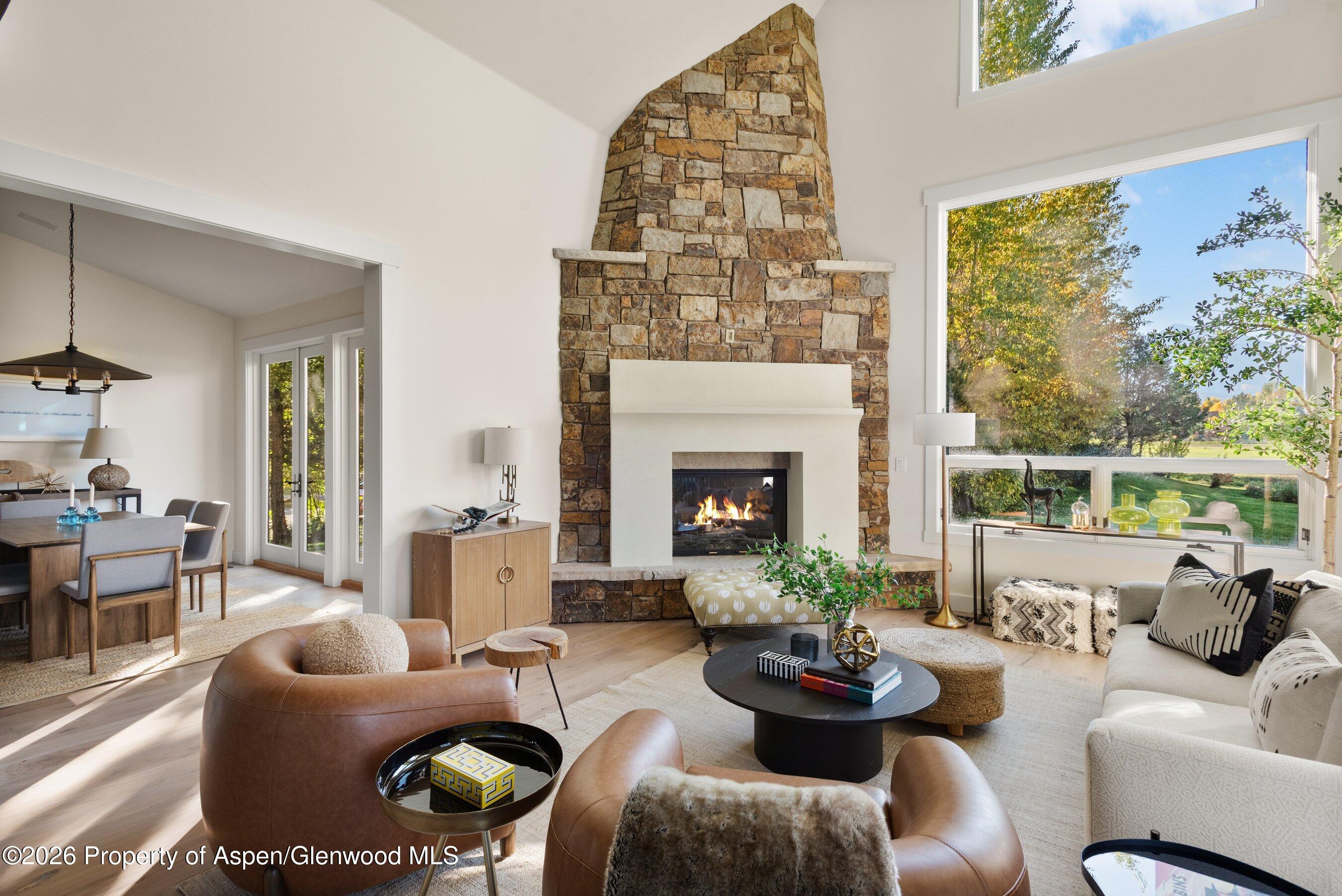 Living room with a tall stone fireplace, large windows, and furnished seating area.