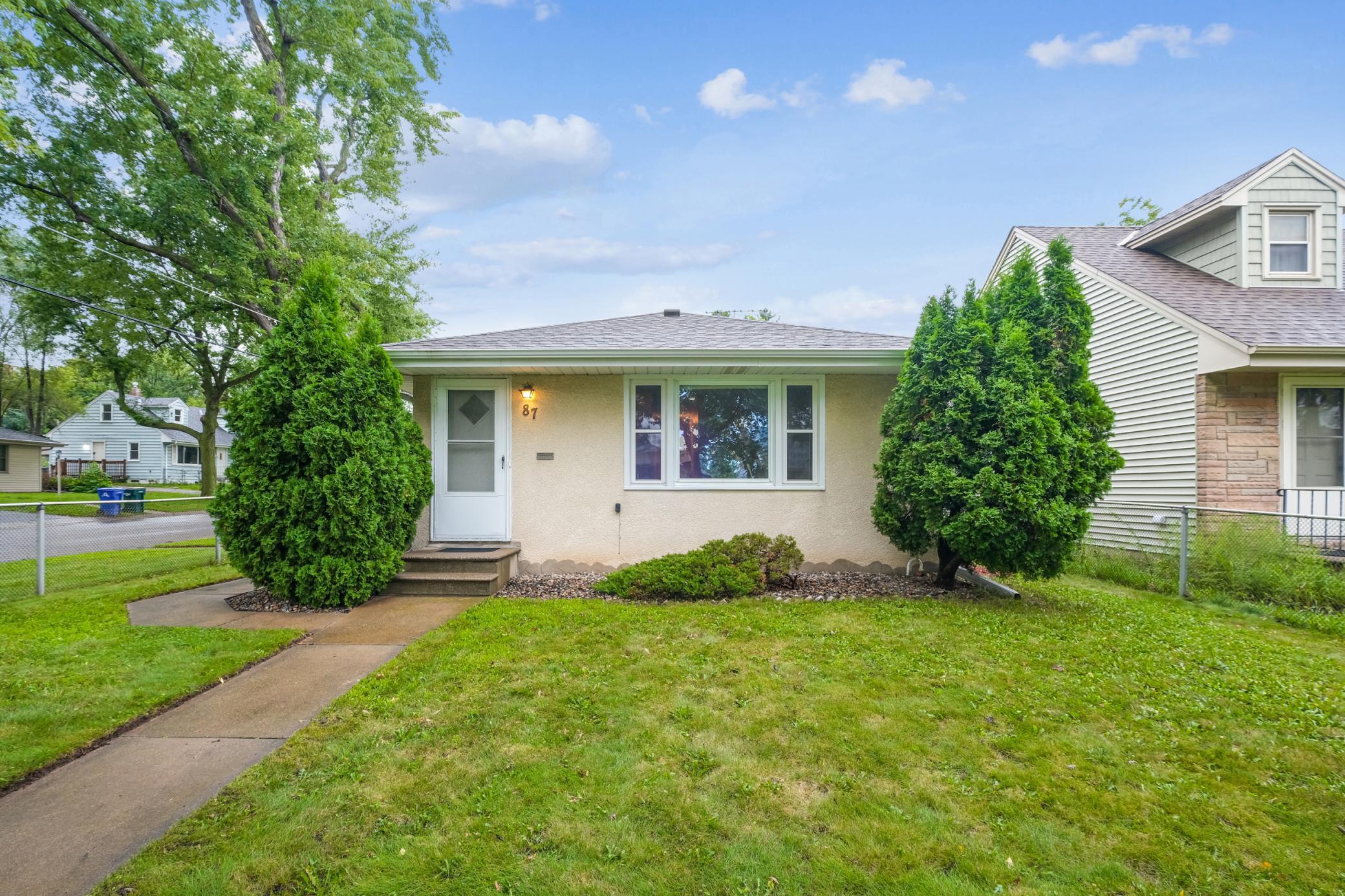 Single-story stucco home with evergreen shrubs flanking the entrance and a walkway across the front lawn.