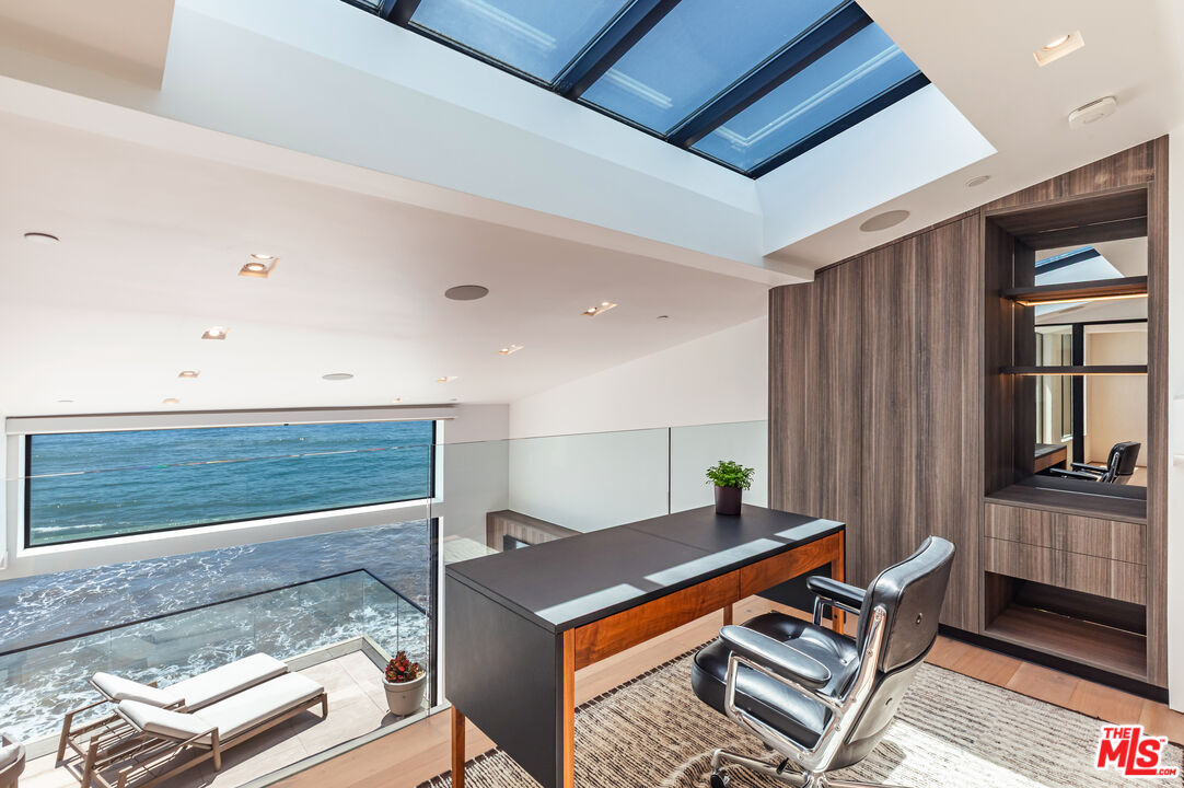 Ocean-view home office with skylights, a dark wood desk, and a leather chair.