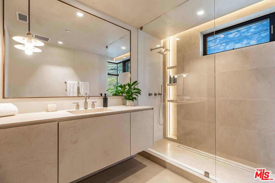 Modern bathroom with a pale stone double vanity and glass-enclosed shower with an illuminated niche.