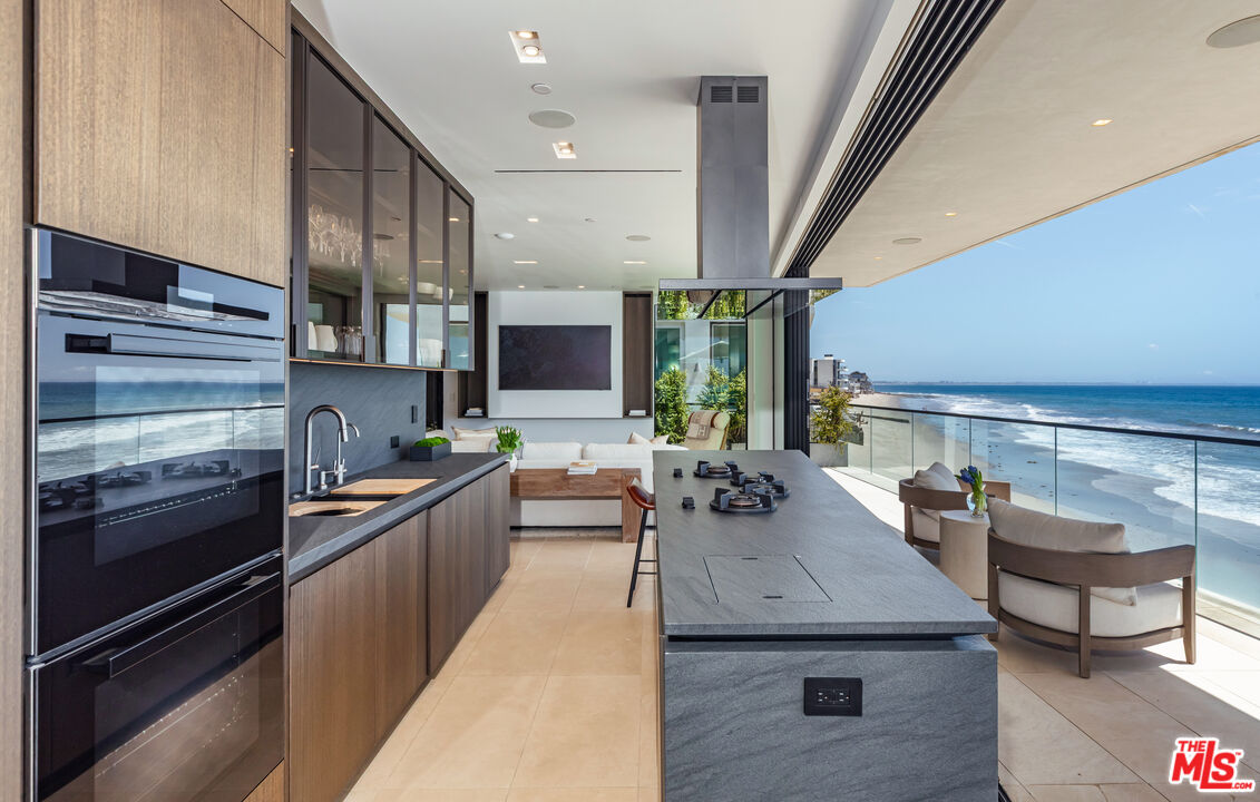 Modern kitchen with a large stone island and ocean views through open glass doors.