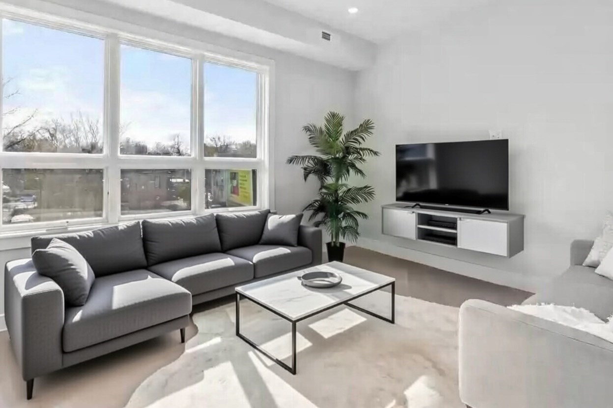 Bright living room with a gray sectional, glass coffee table, and large windows overlooking a snowy street.