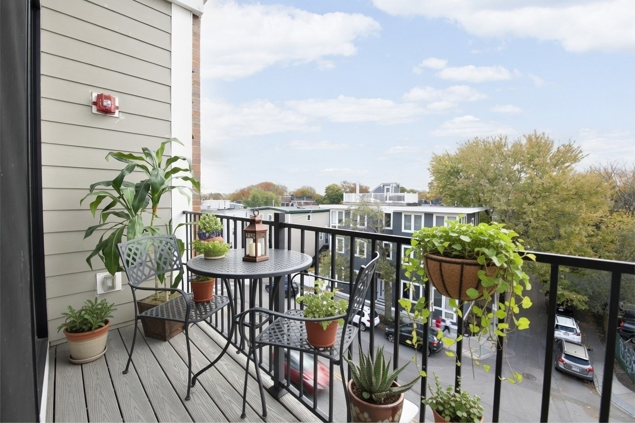 Apartment balcony with a bistro table and potted plants overlooking neighboring buildings.