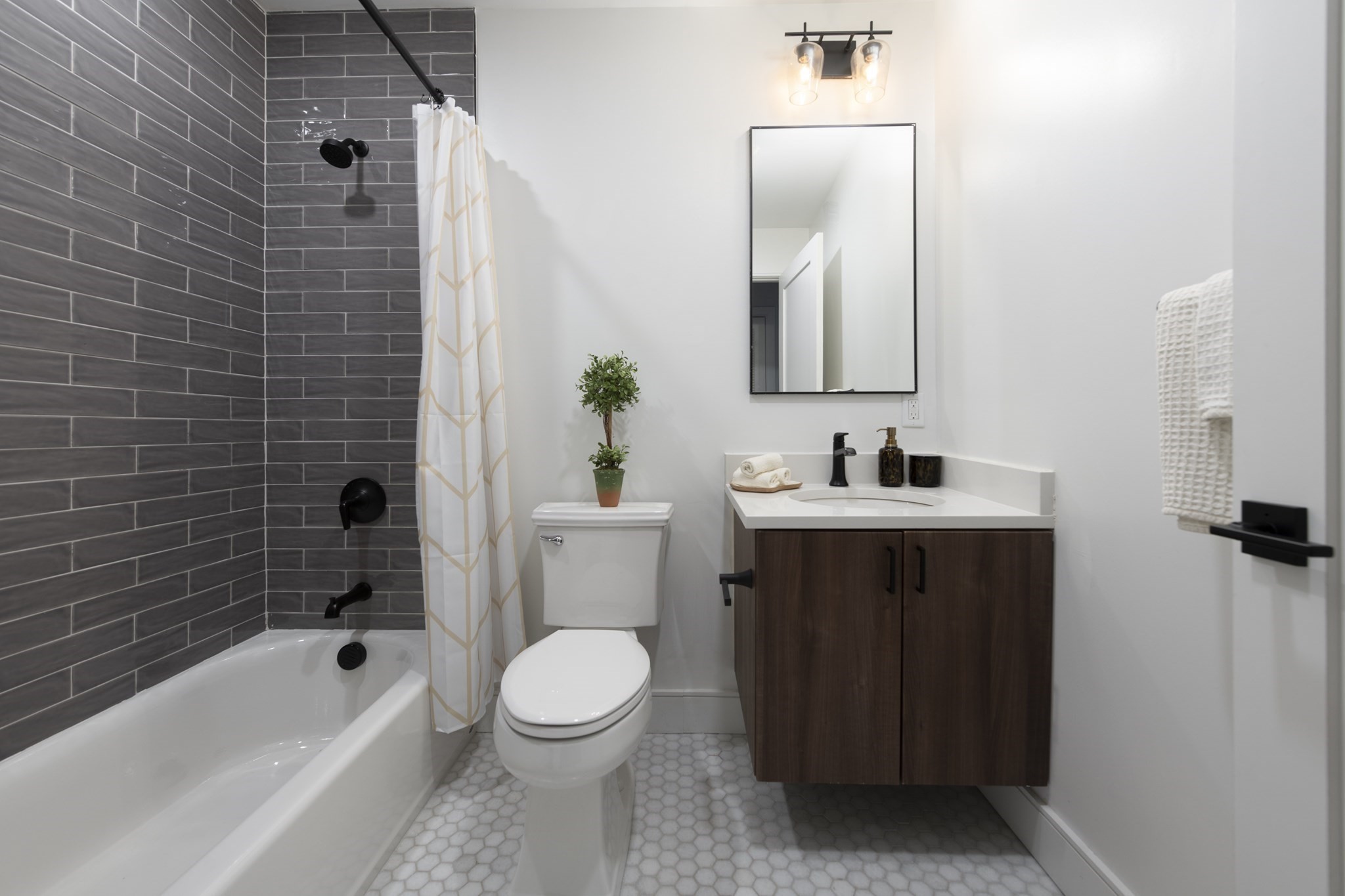 Bathroom with a dark tiled tub surround, geometric shower curtain, and dark wood vanity.