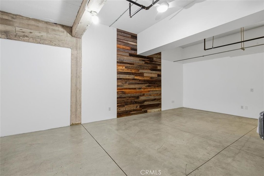 Vacant room with polished concrete floors, a reclaimed wood accent wall, and exposed concrete beams.