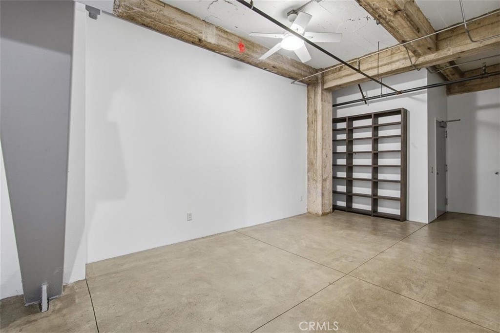 Vacant loft-style room with exposed beams, concrete floor, ceiling fan, and built-in shelving.