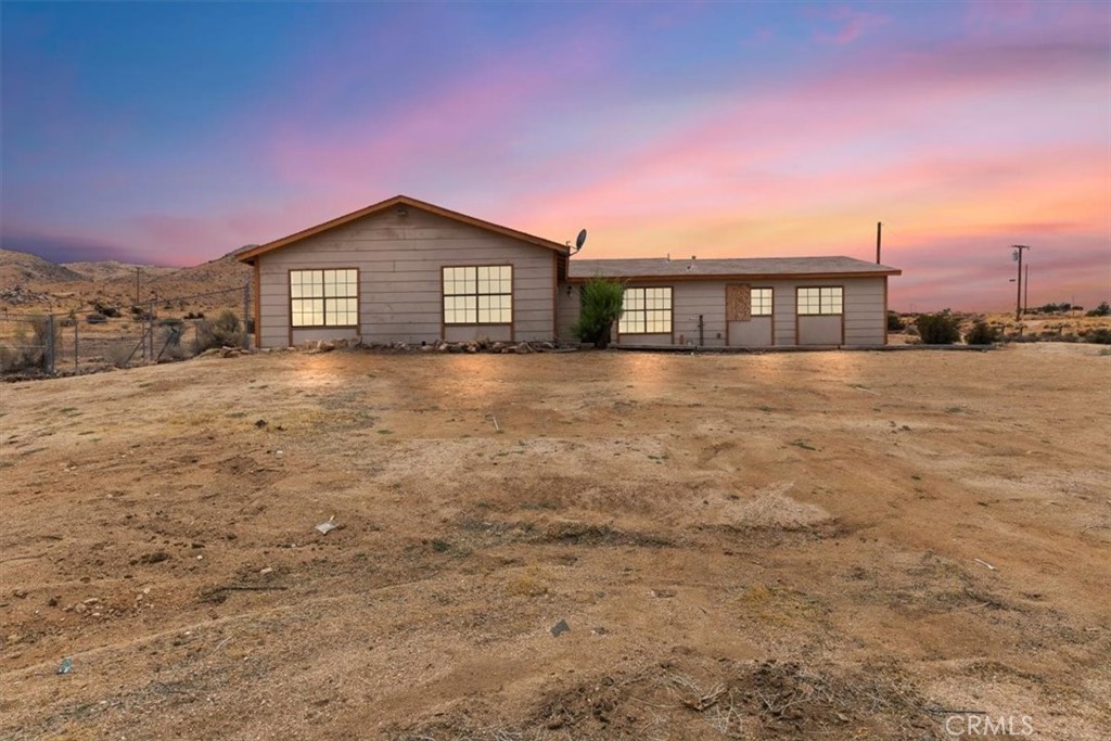 Single-story gray house on a wide dirt lot, with rocky hills and a pink dusk sky.