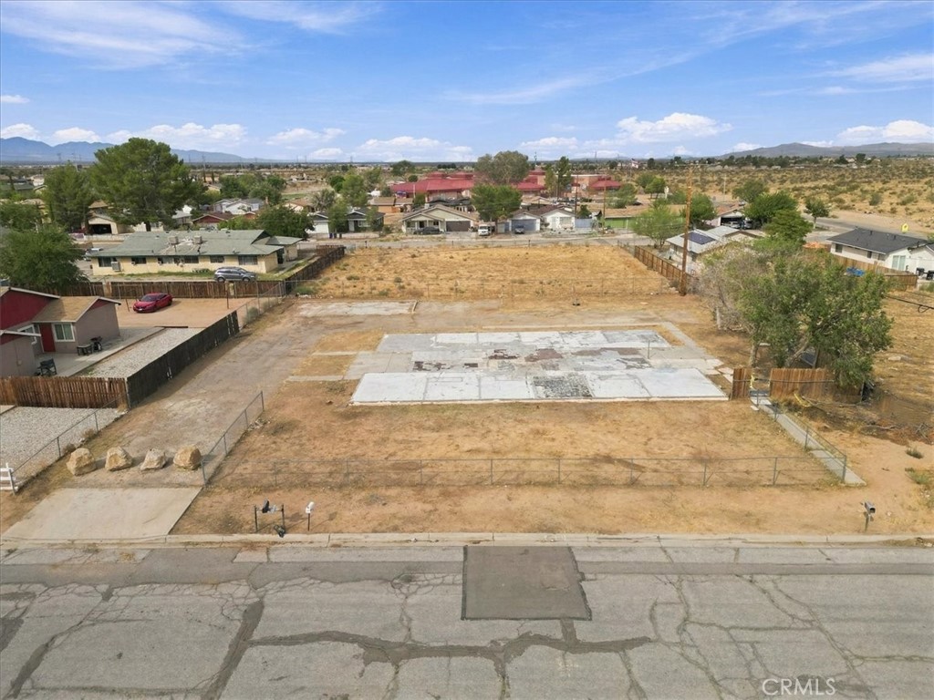 Fenced vacant lot with a concrete slab, neighboring homes, and distant mountains.