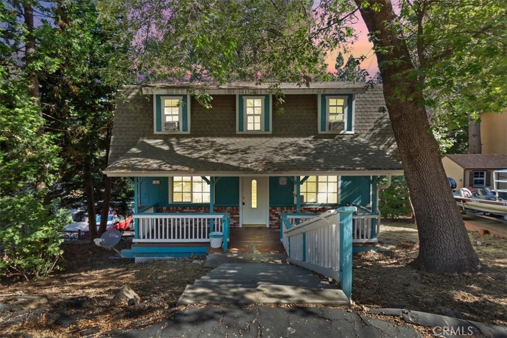 Two-story teal house with a covered porch and walkway, shaded by mature trees.