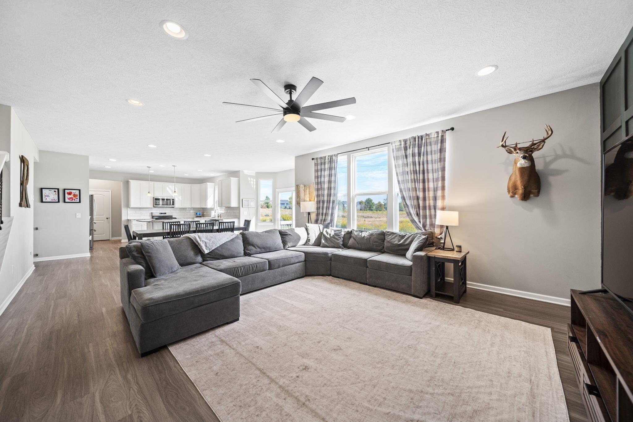 Open-plan living room with a large gray sectional, tall curtained windows, and kitchen beyond.