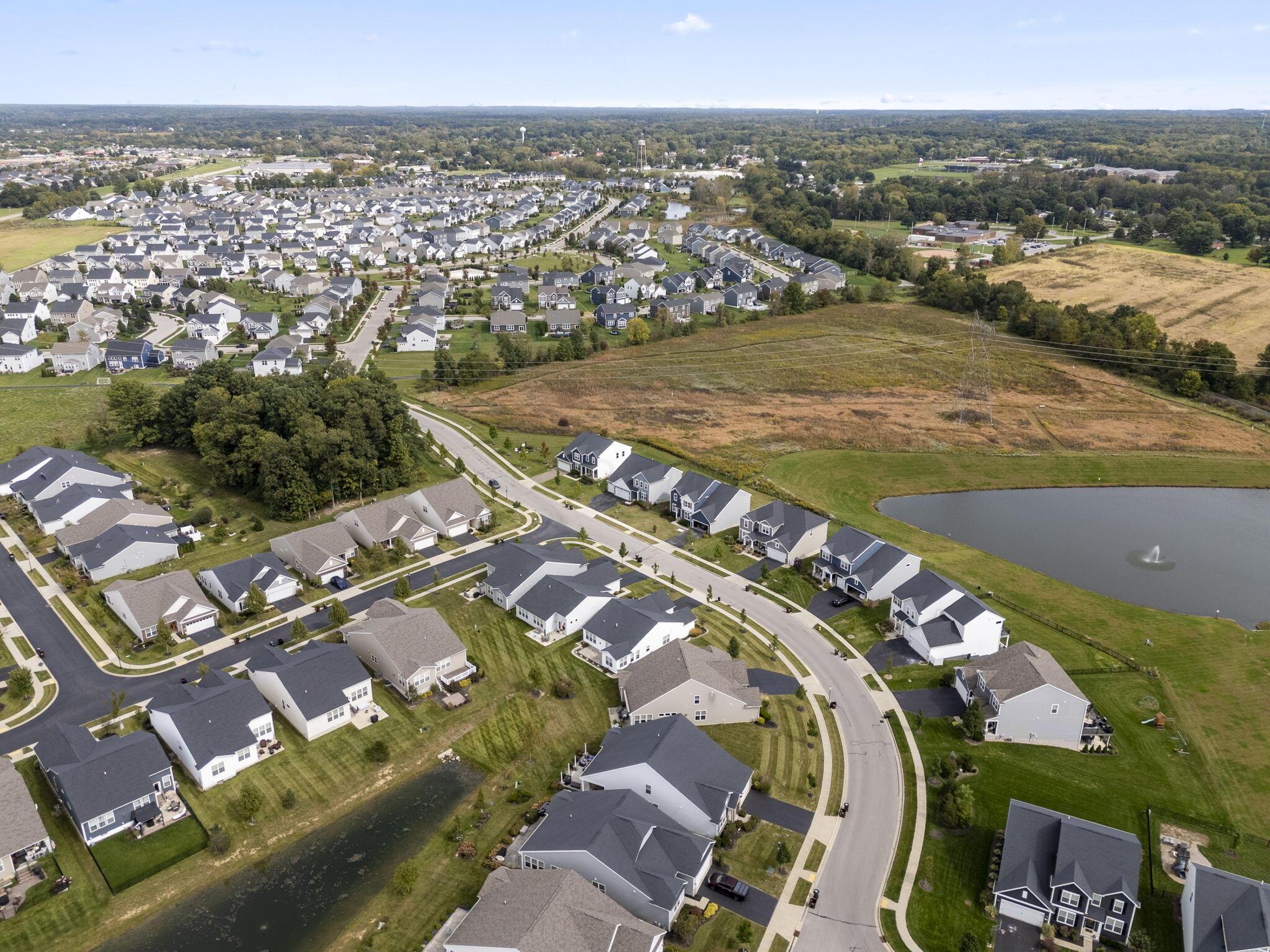 Aerial view of a residential neighborhood with curving streets, a pond, and surrounding fields.