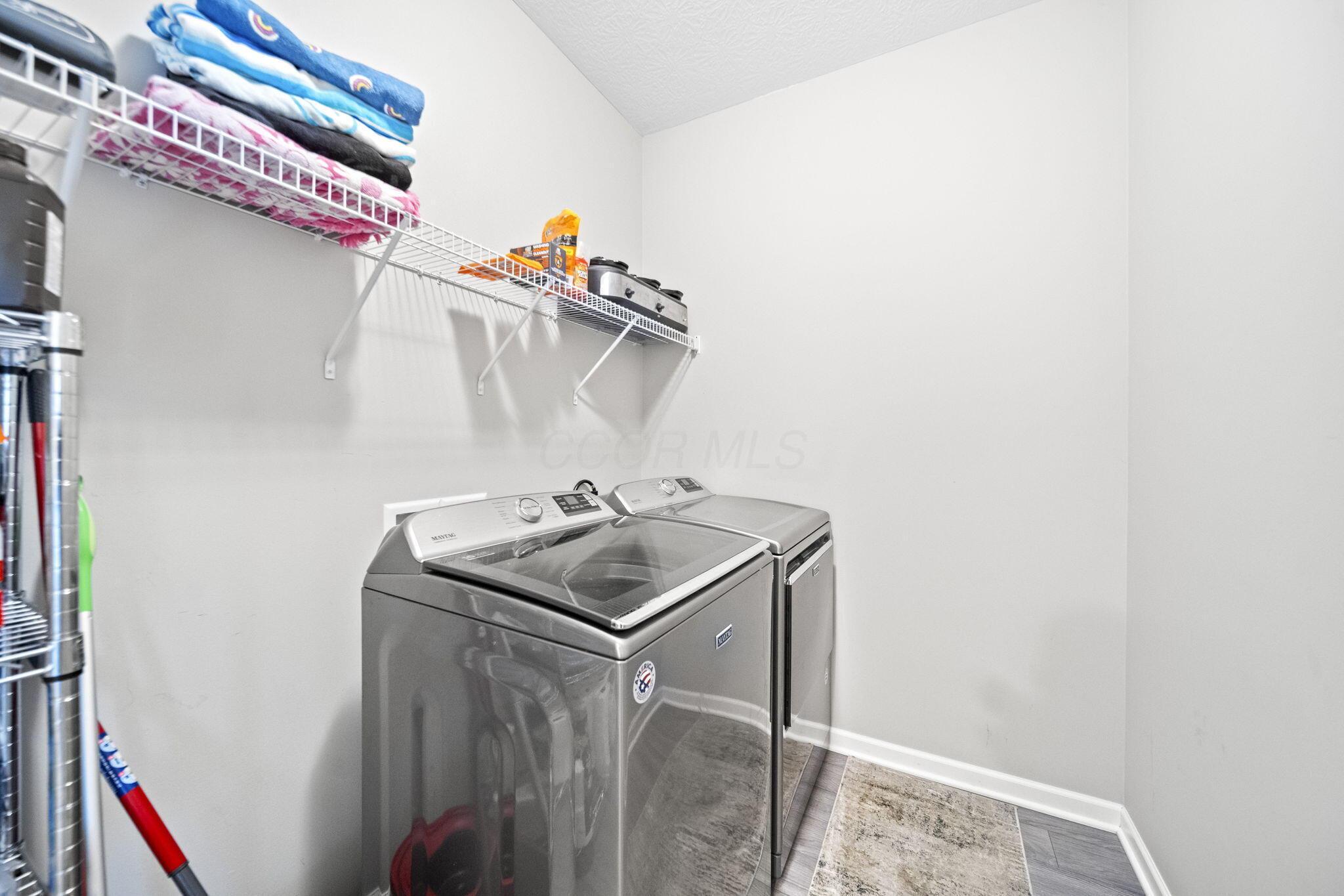 Laundry room with gray washer and dryer beneath wire shelves stocked with towels and supplies.