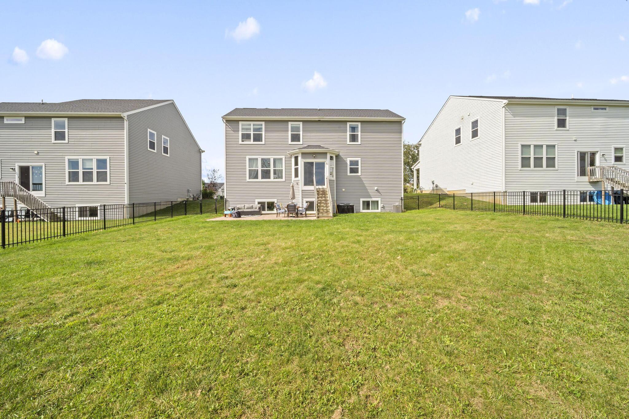 Rear of a two-story home with a fenced lawn and small patio with outdoor seating.