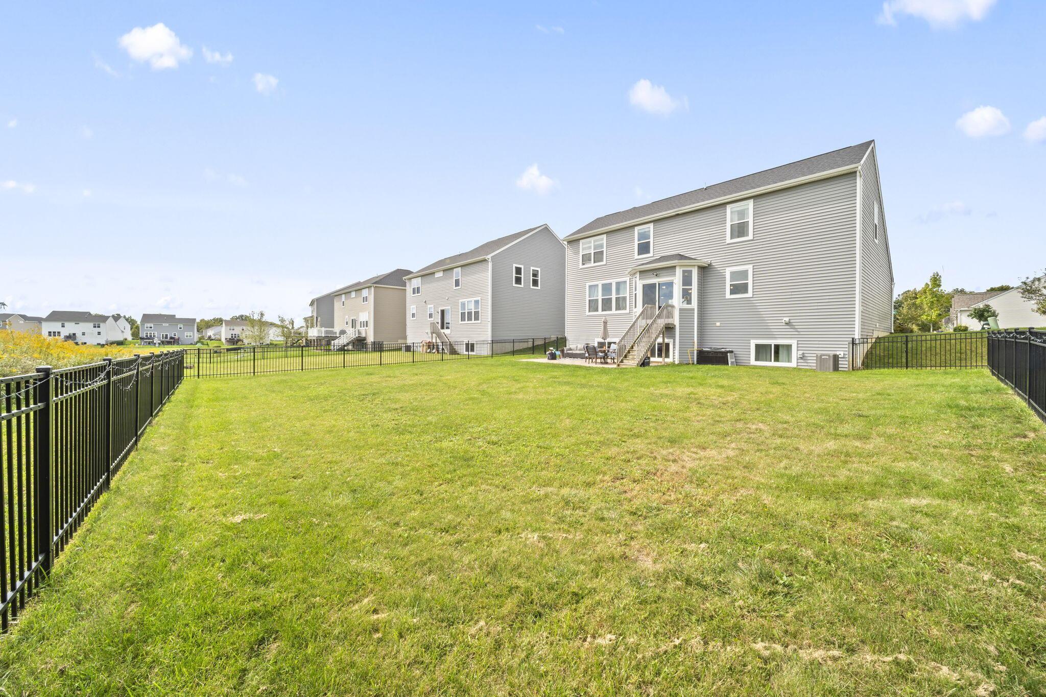 Gray two-story house behind a spacious fenced lawn, with patio furniture by the back steps.