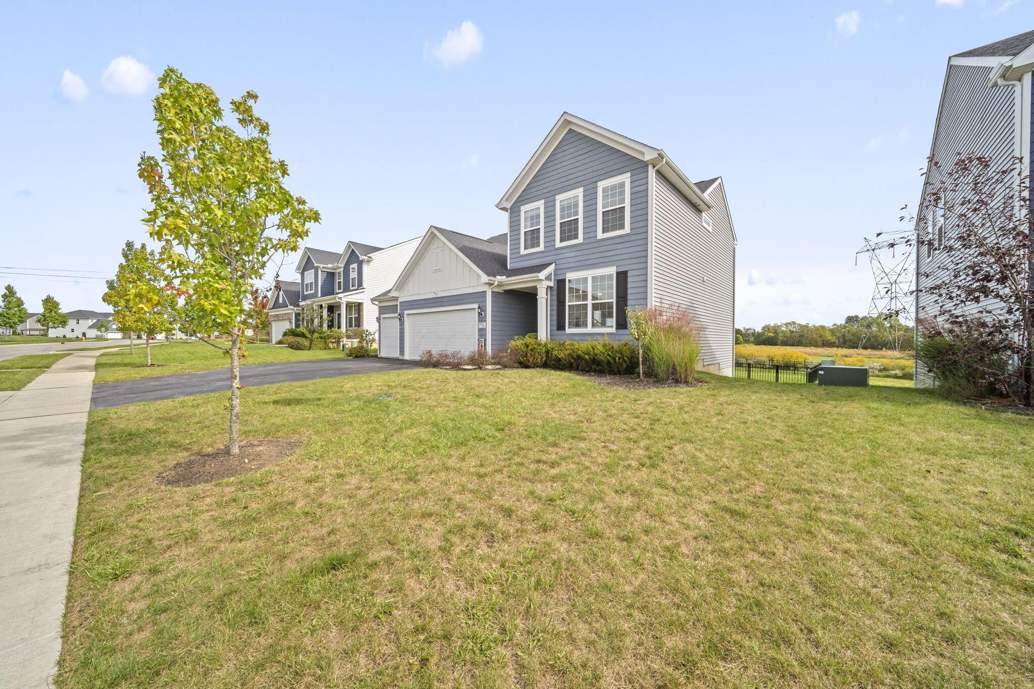 Blue-gray two-story house with a two-car garage, broad front lawn, and young trees.