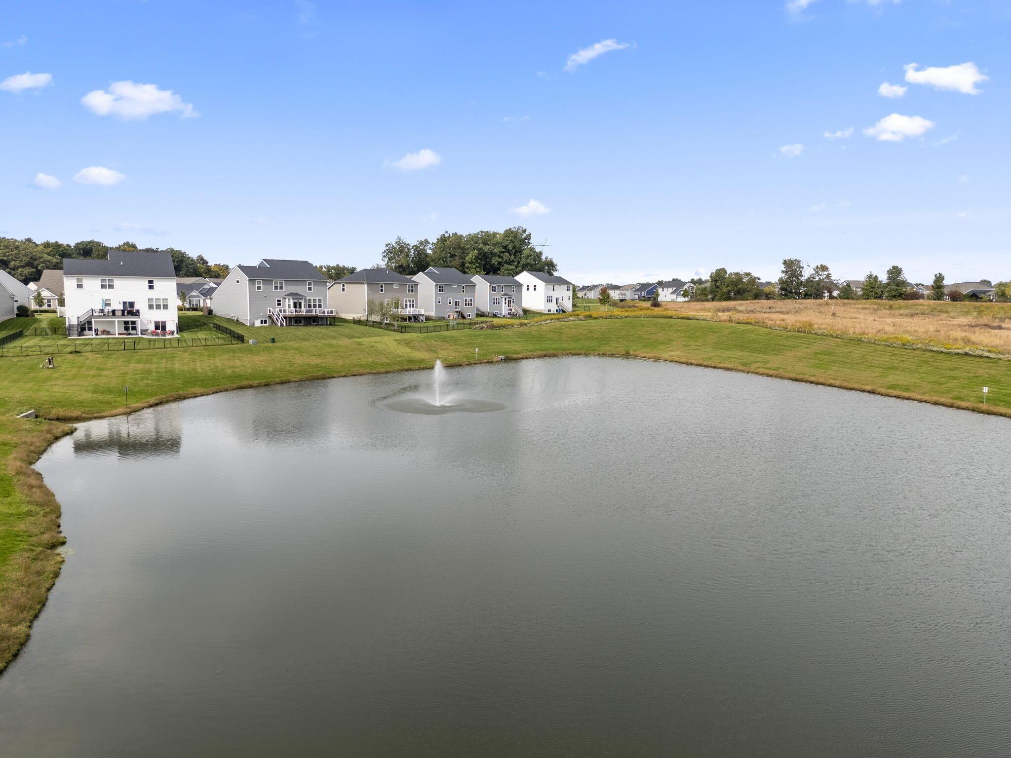 Aerial view of a neighborhood pond with a fountain and homes along the shore.