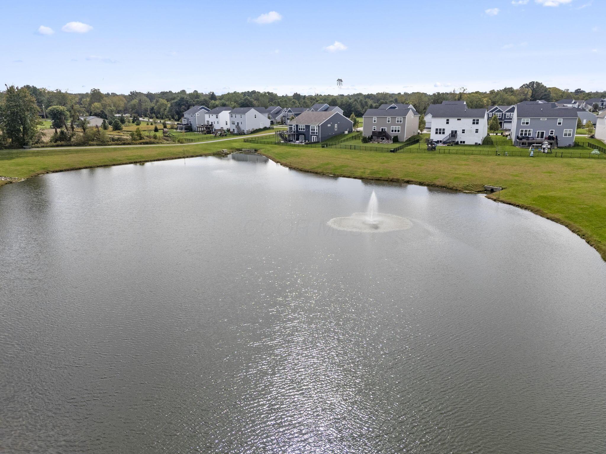 Aerial view of a neighborhood pond with a fountain and homes along its banks.