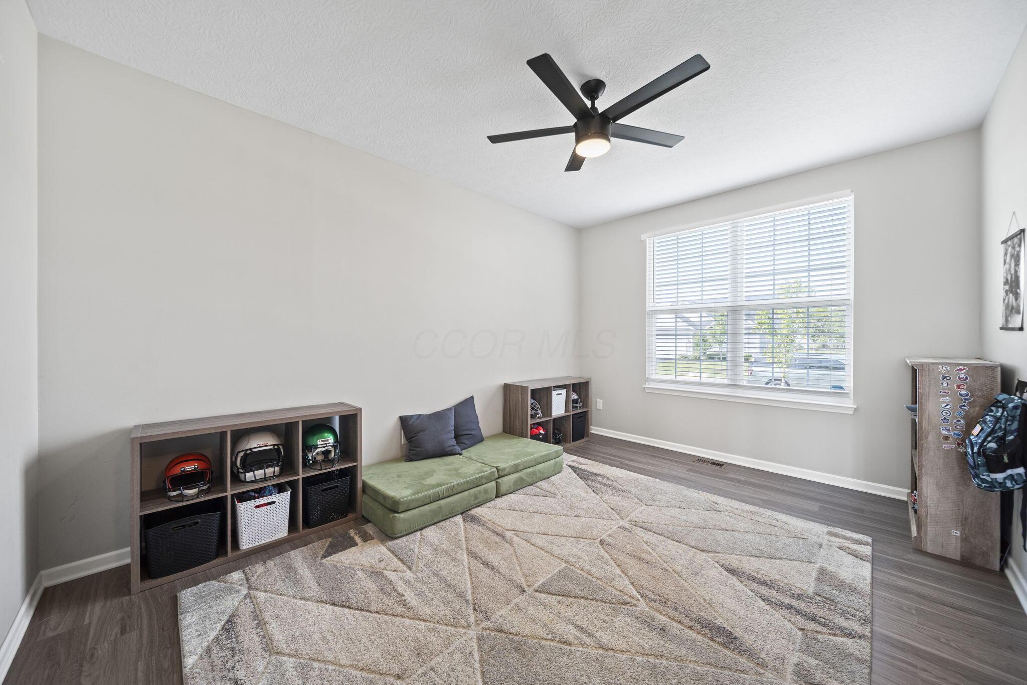 Furnished bedroom with a green floor cushion, sports equipment cubbies, and a large window with blinds.
