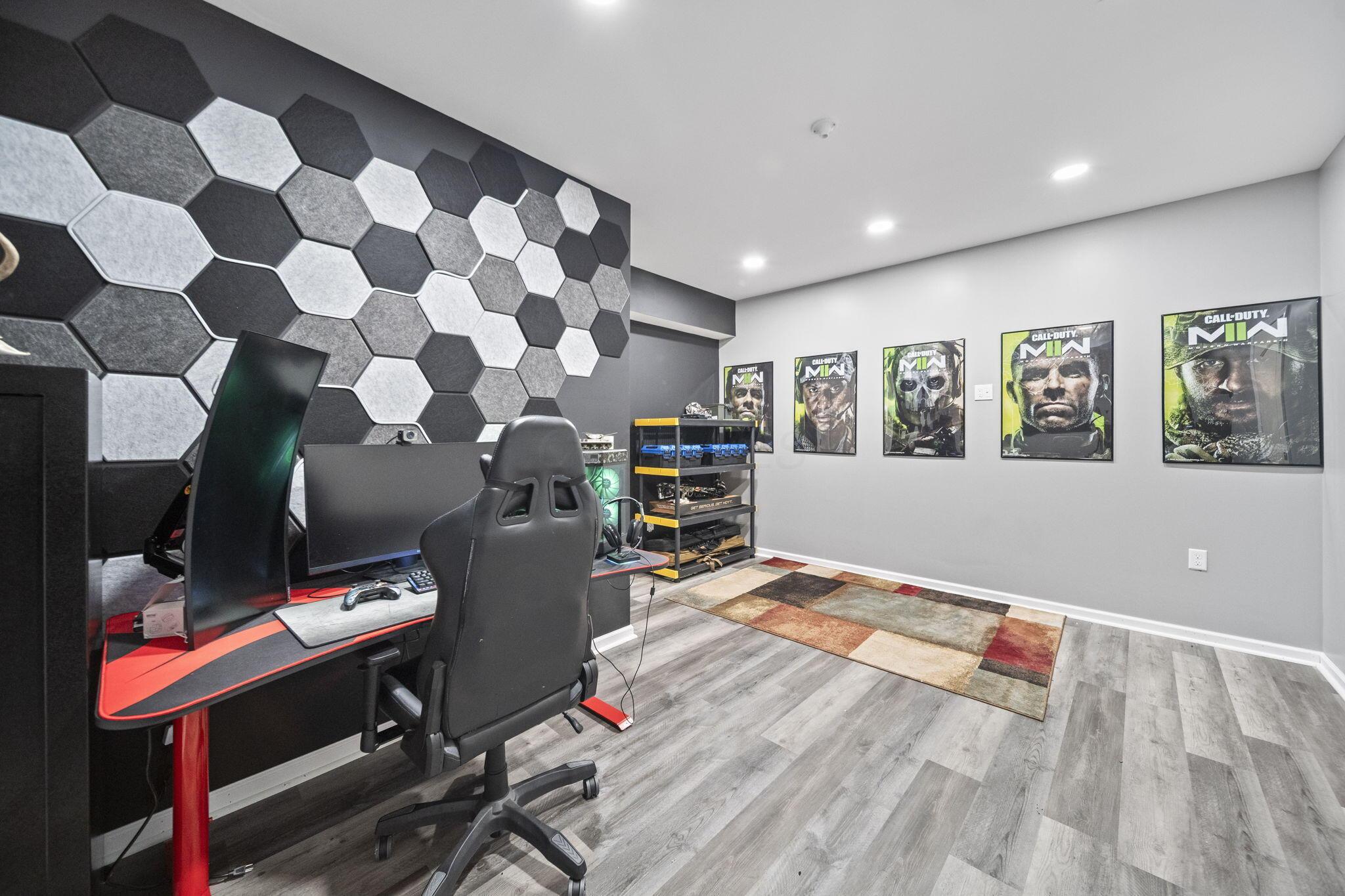 Gaming room with a computer setup, hexagonal wall panels, Call of Duty posters and a patchwork rug.