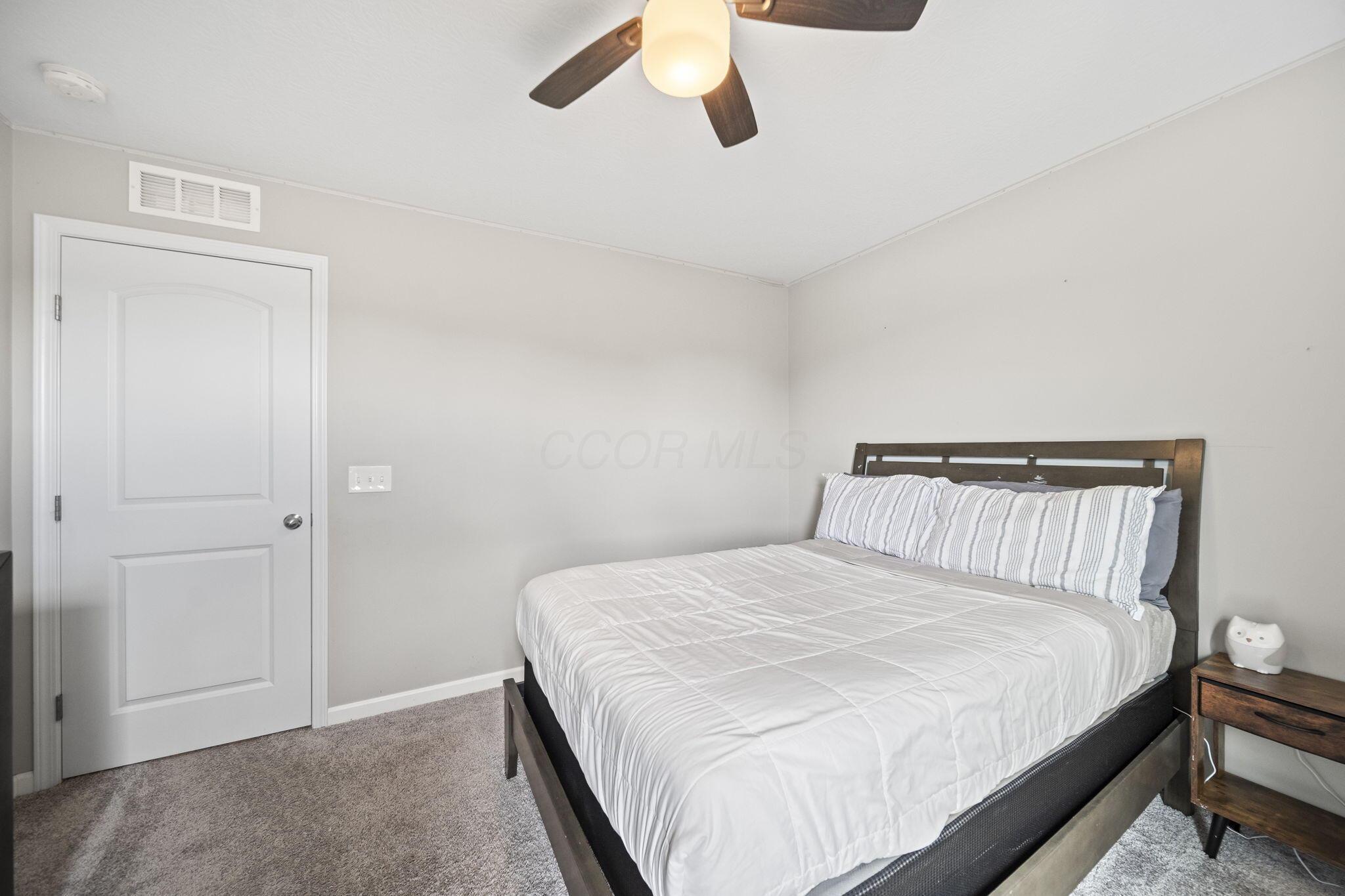 Bedroom with a dark wood bed, white striped pillows, gray carpet, and ceiling fan.