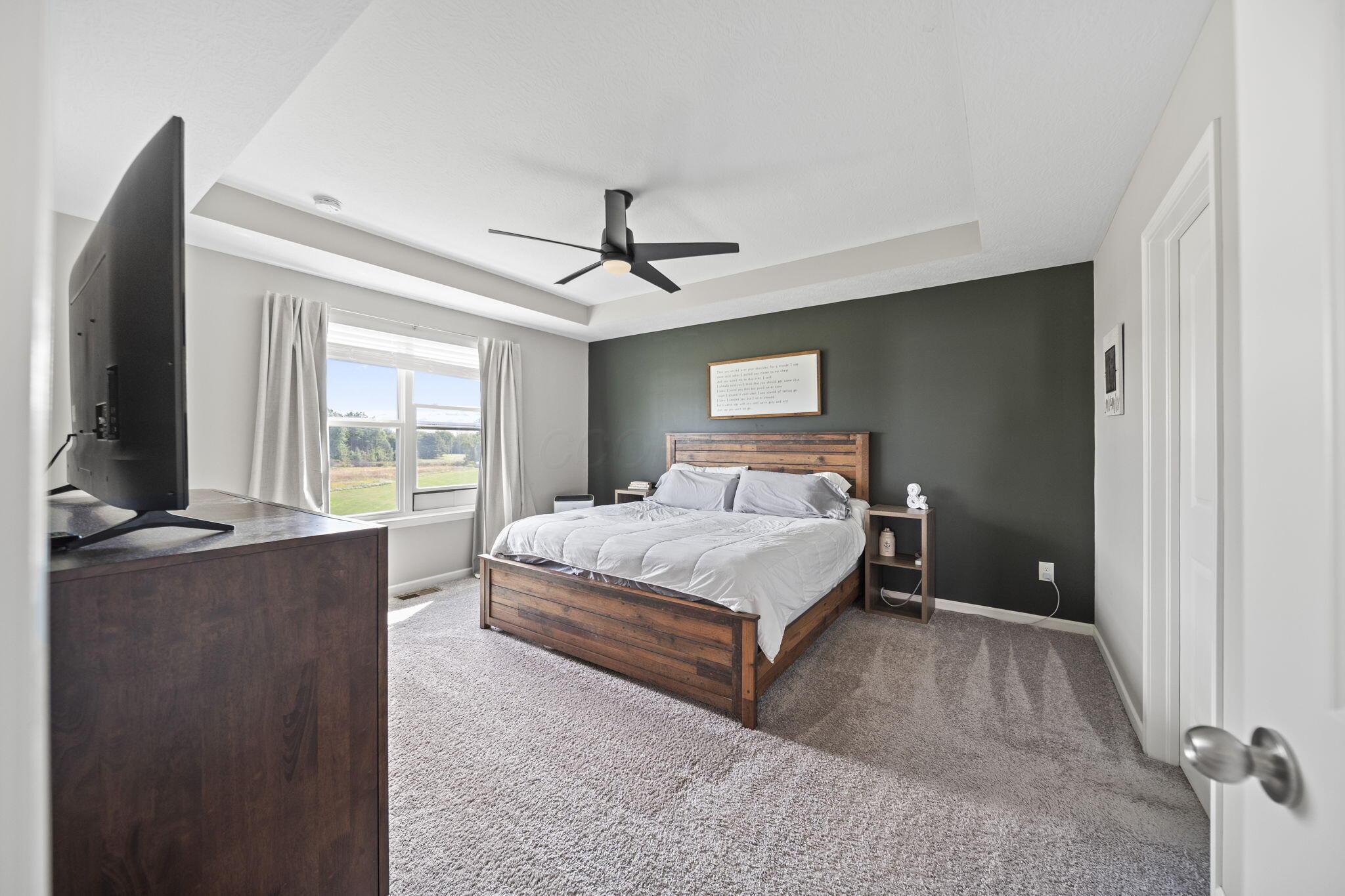 Bedroom with a wooden bed against a dark accent wall and a window overlooking an open field.