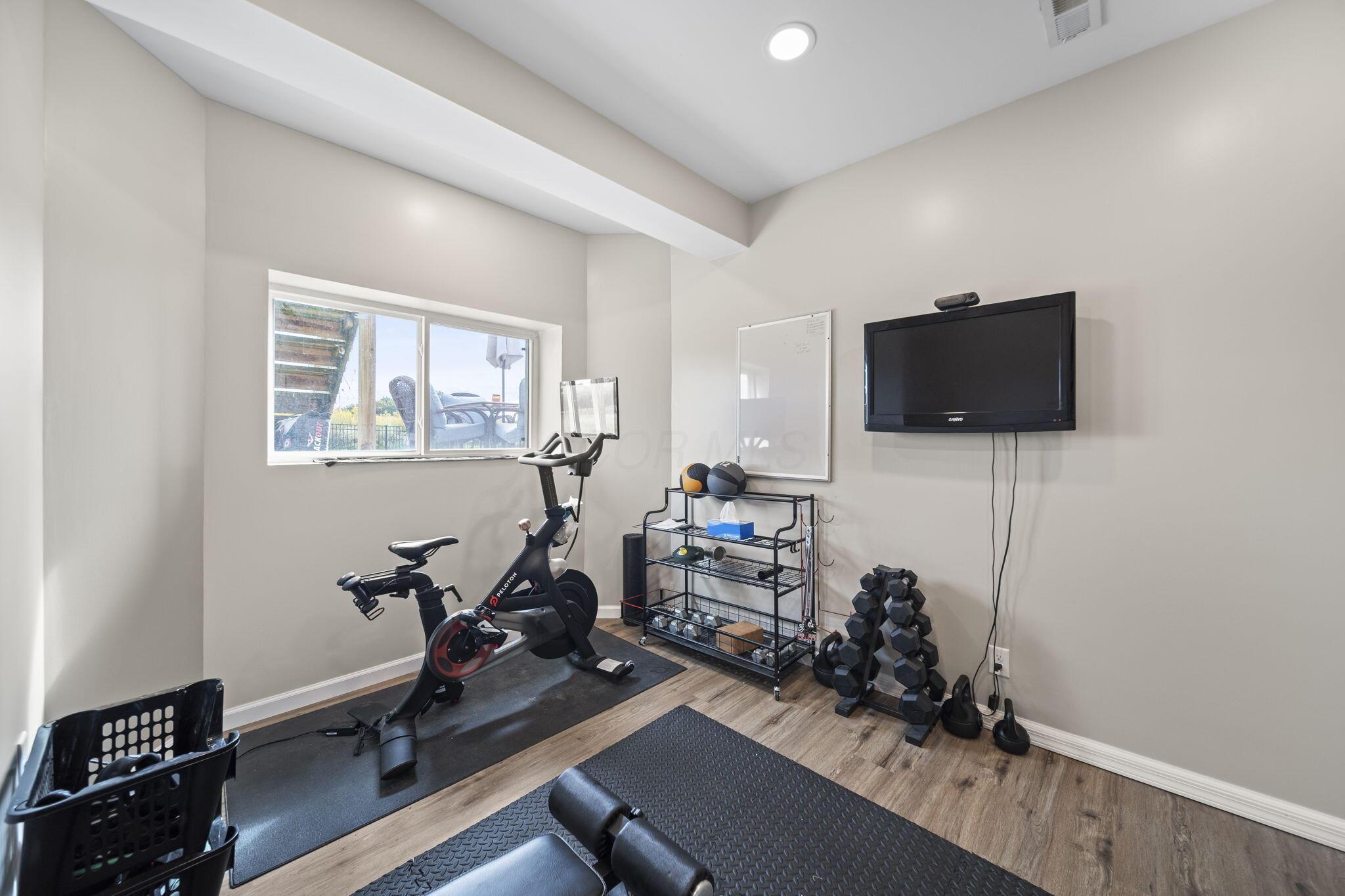 Home gym with stationary bikes, dumbbells, workout mats, and a wall-mounted television.