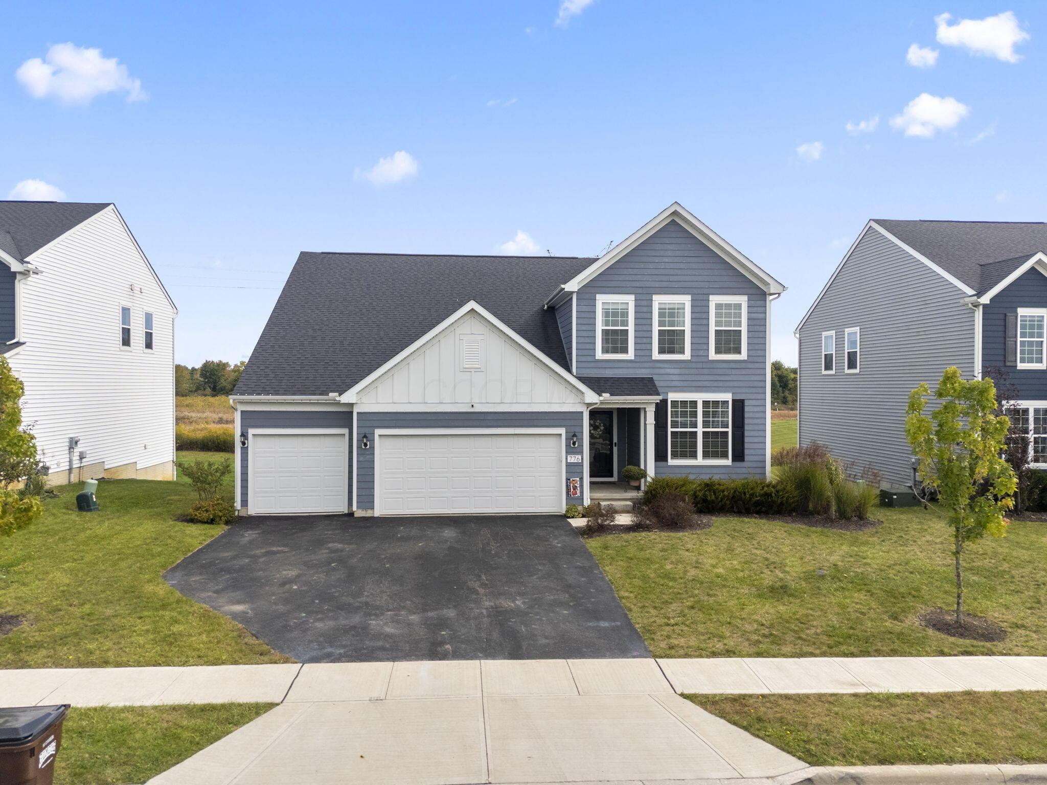 Blue-gray two-story house with white trim, an attached two-car garage, and a broad paved driveway.