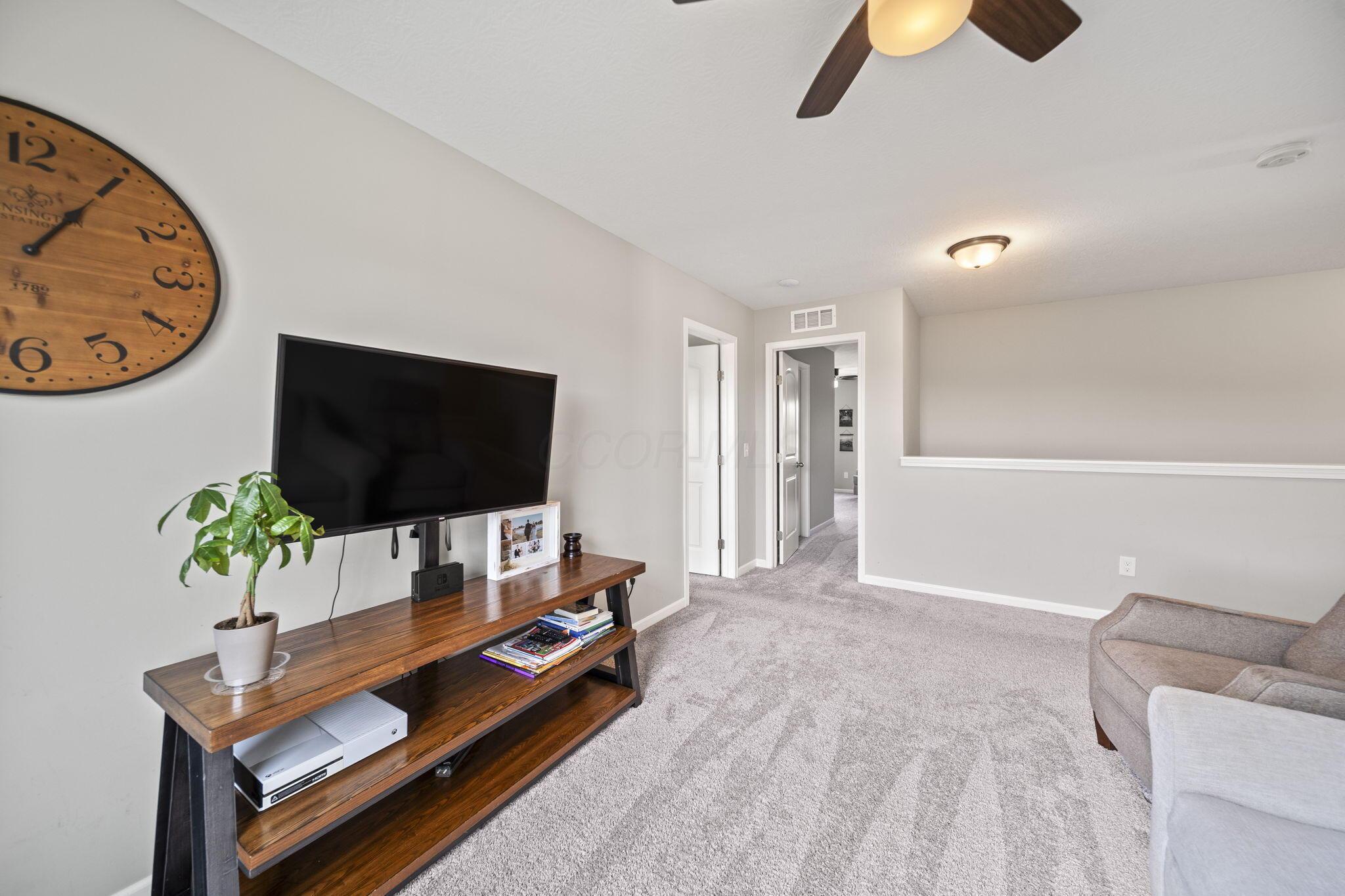 Carpeted sitting room with a television, wood media console, and ceiling fan.