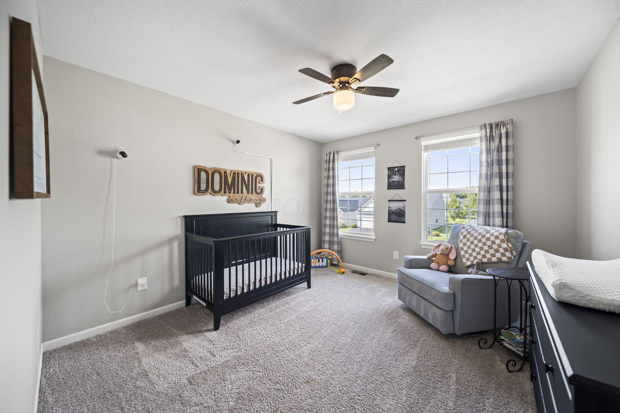 Nursery with a black crib, gray armchair, plush toys, and two curtained windows.