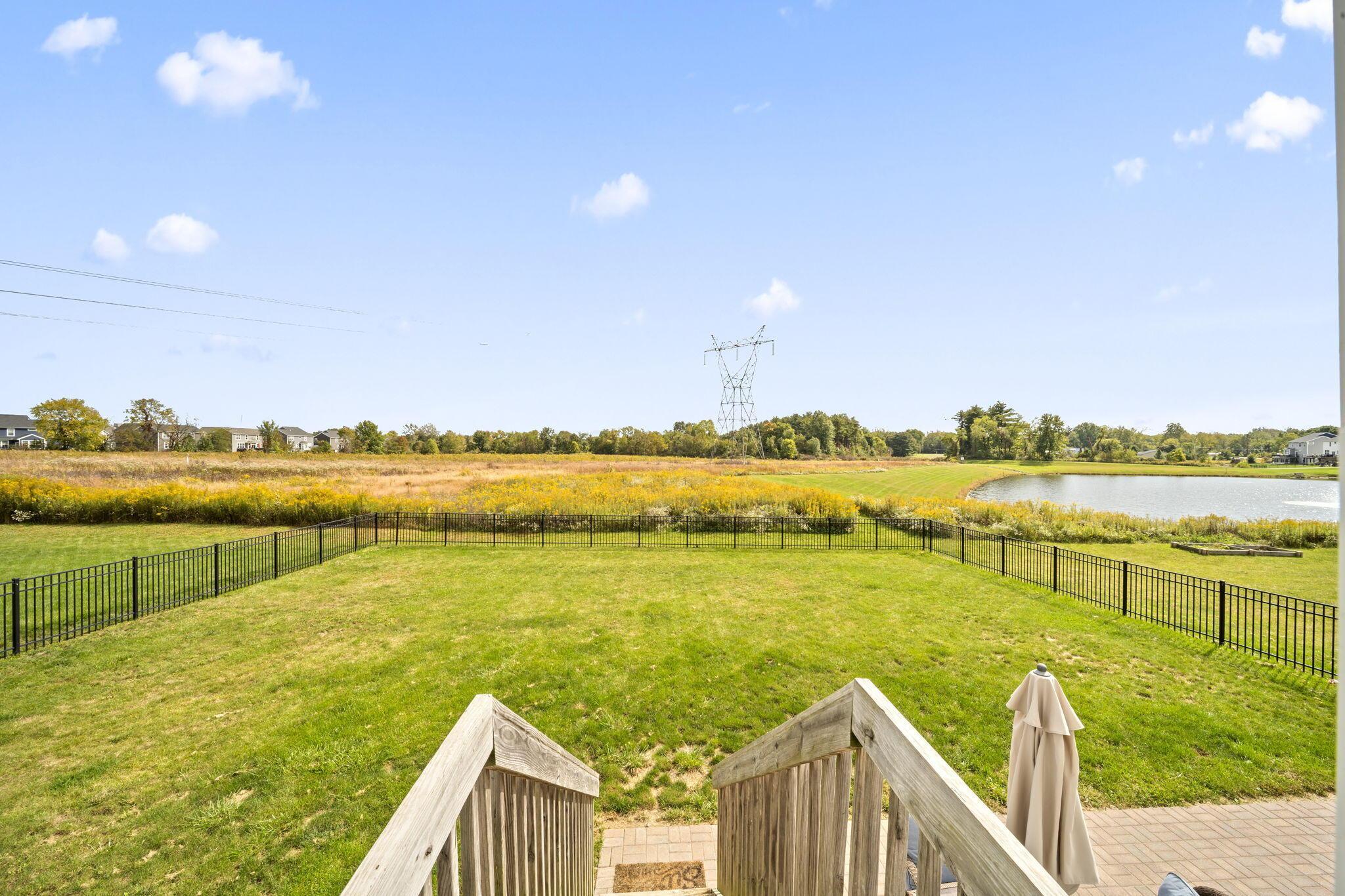 Fenced backyard lawn overlooking a pond and autumn meadow, viewed from a wooden deck.