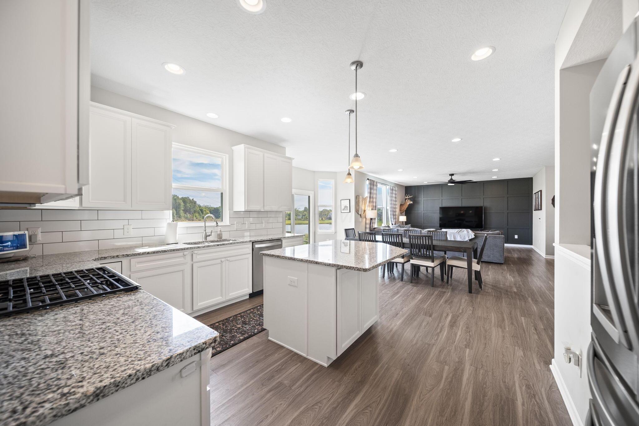 Open kitchen with granite island, white cabinets, and adjoining dining and living areas.