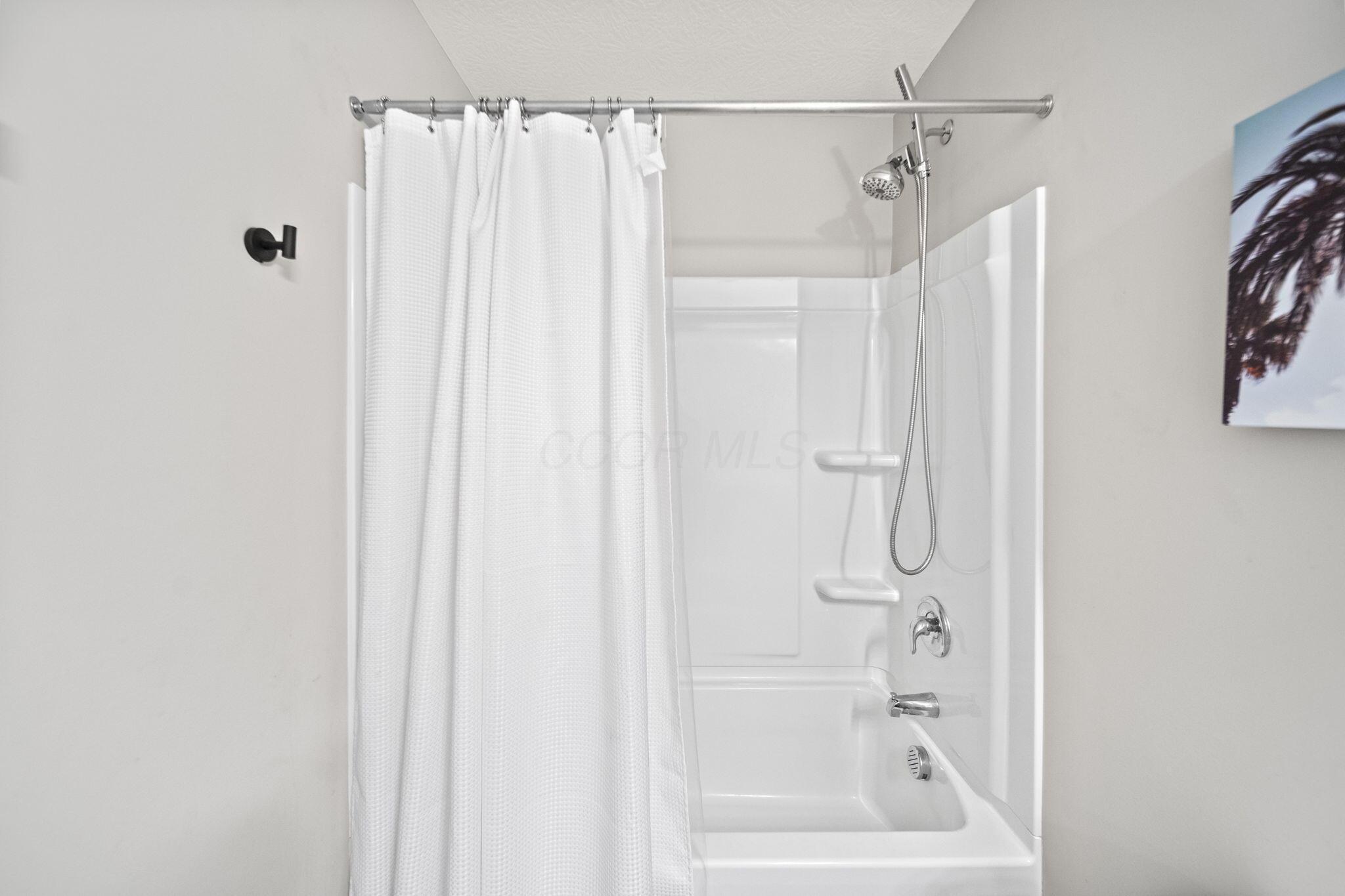 Bathroom tub and shower with a white curtain and handheld showerhead.