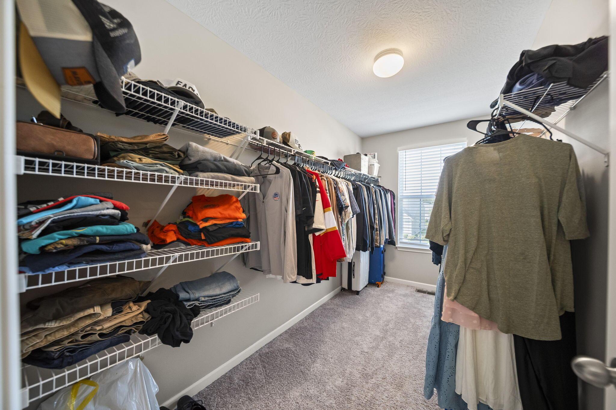 Walk-in closet with extensive clothing storage, wire shelving, hanging clothes, and a window with blinds.