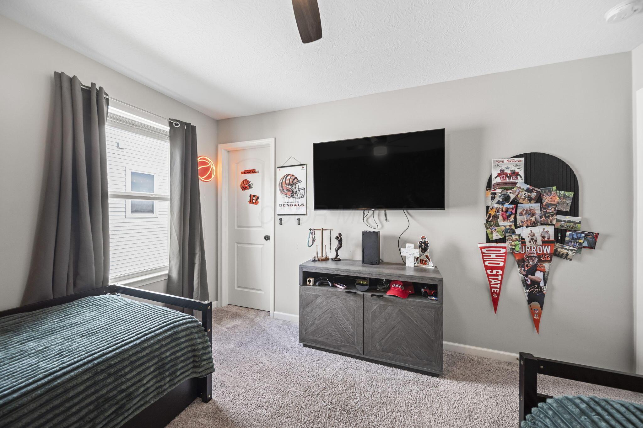 Bedroom with two beds, a wall-mounted TV, and Cincinnati Bengals and Ohio State memorabilia.