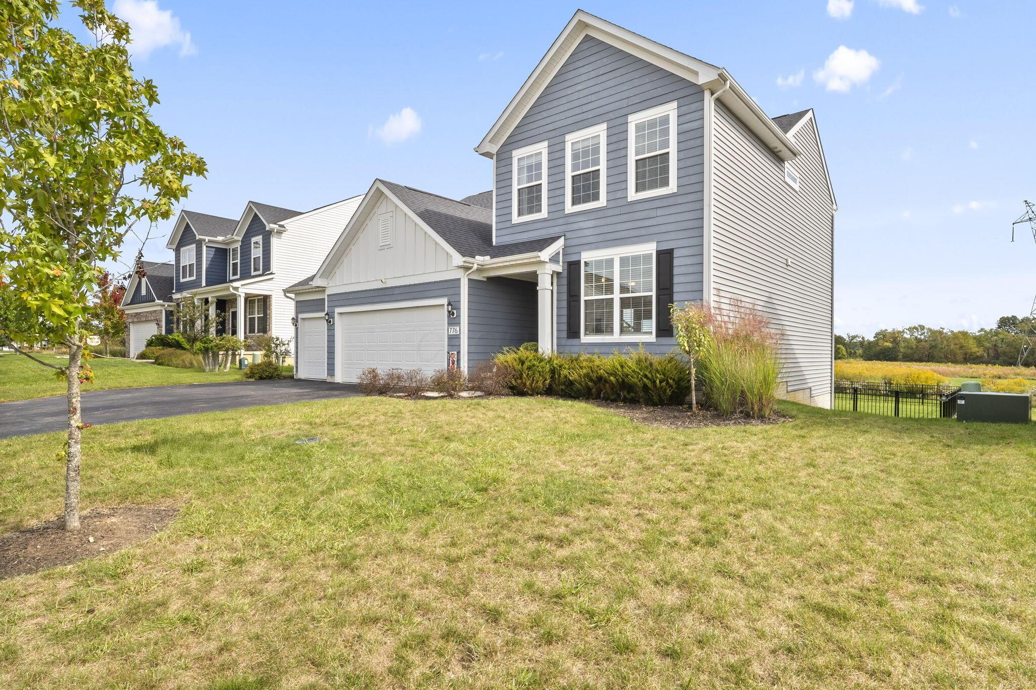 Two-story gray house with an attached double garage, broad lawn, and fenced field behind it.