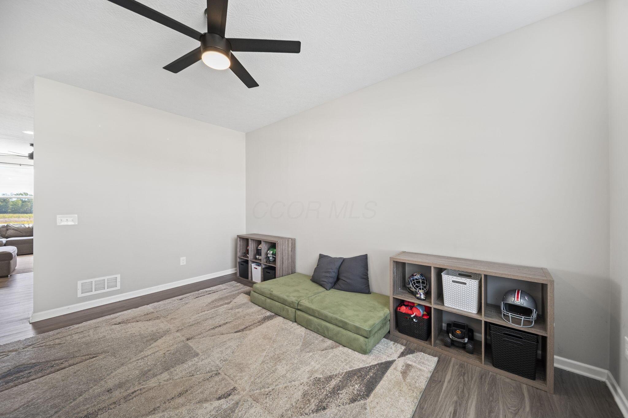Furnished room with sports-equipment cubbies, a green floor cushion, and a black ceiling fan.