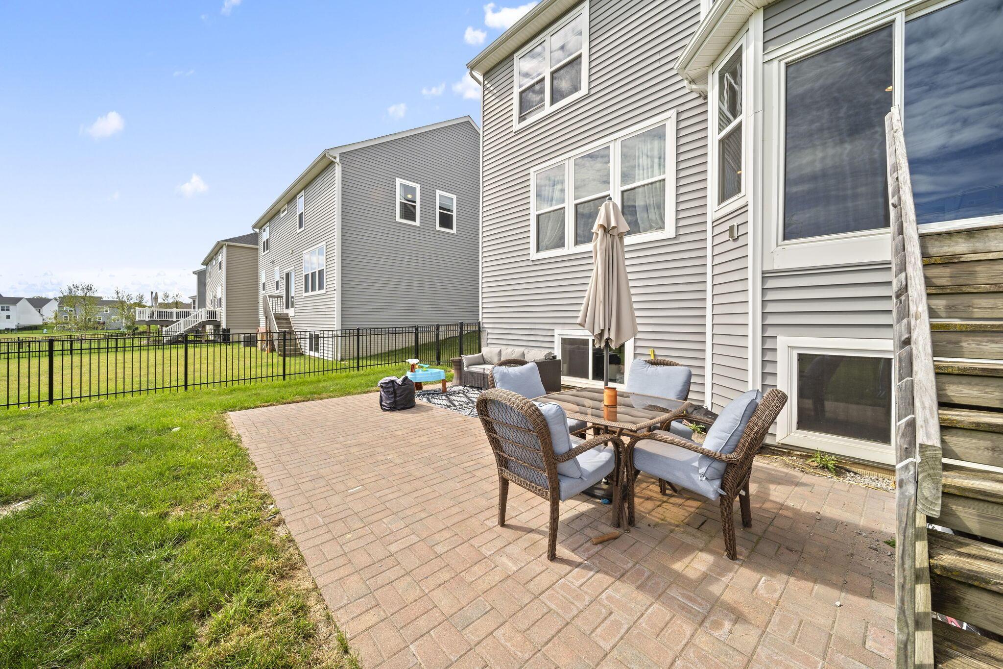 Rear patio with wicker seating, brick pavers, and a fenced lawn beside a gray-sided home.