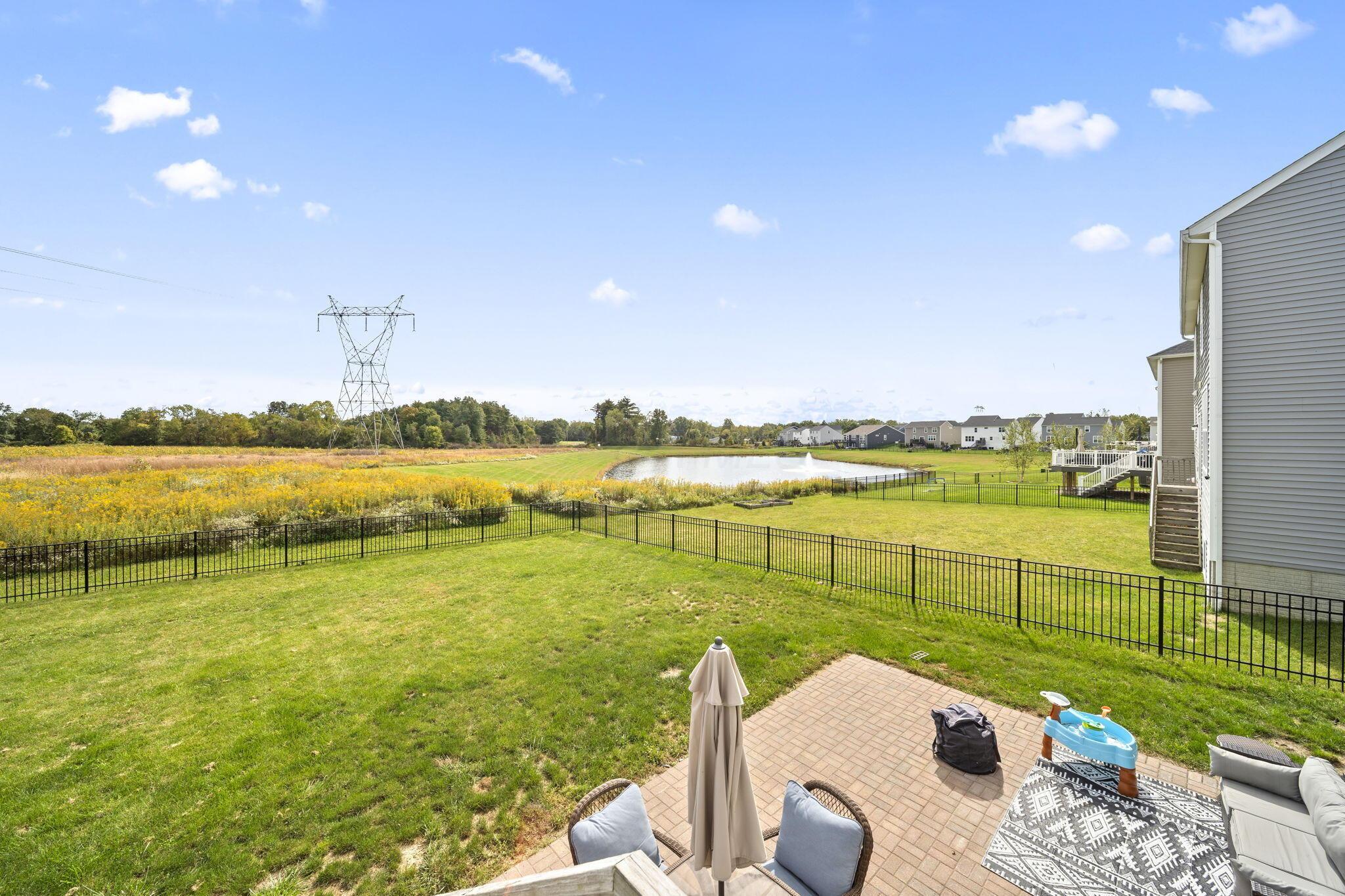 Fenced backyard and brick patio overlook a pond, meadow, and neighboring homes.