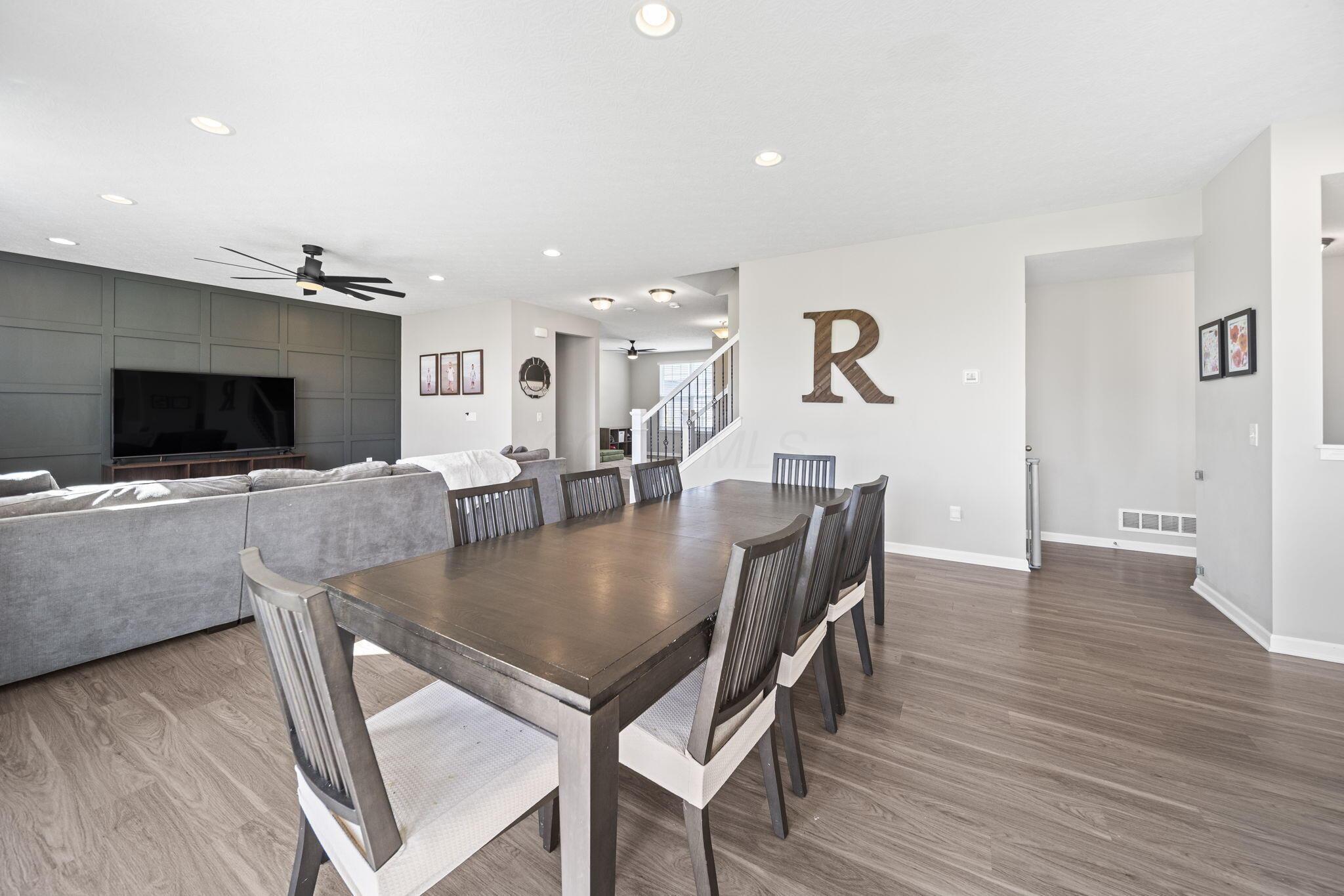 Open-plan dining and living area with a dark wood table, gray sectional, and paneled television wall.