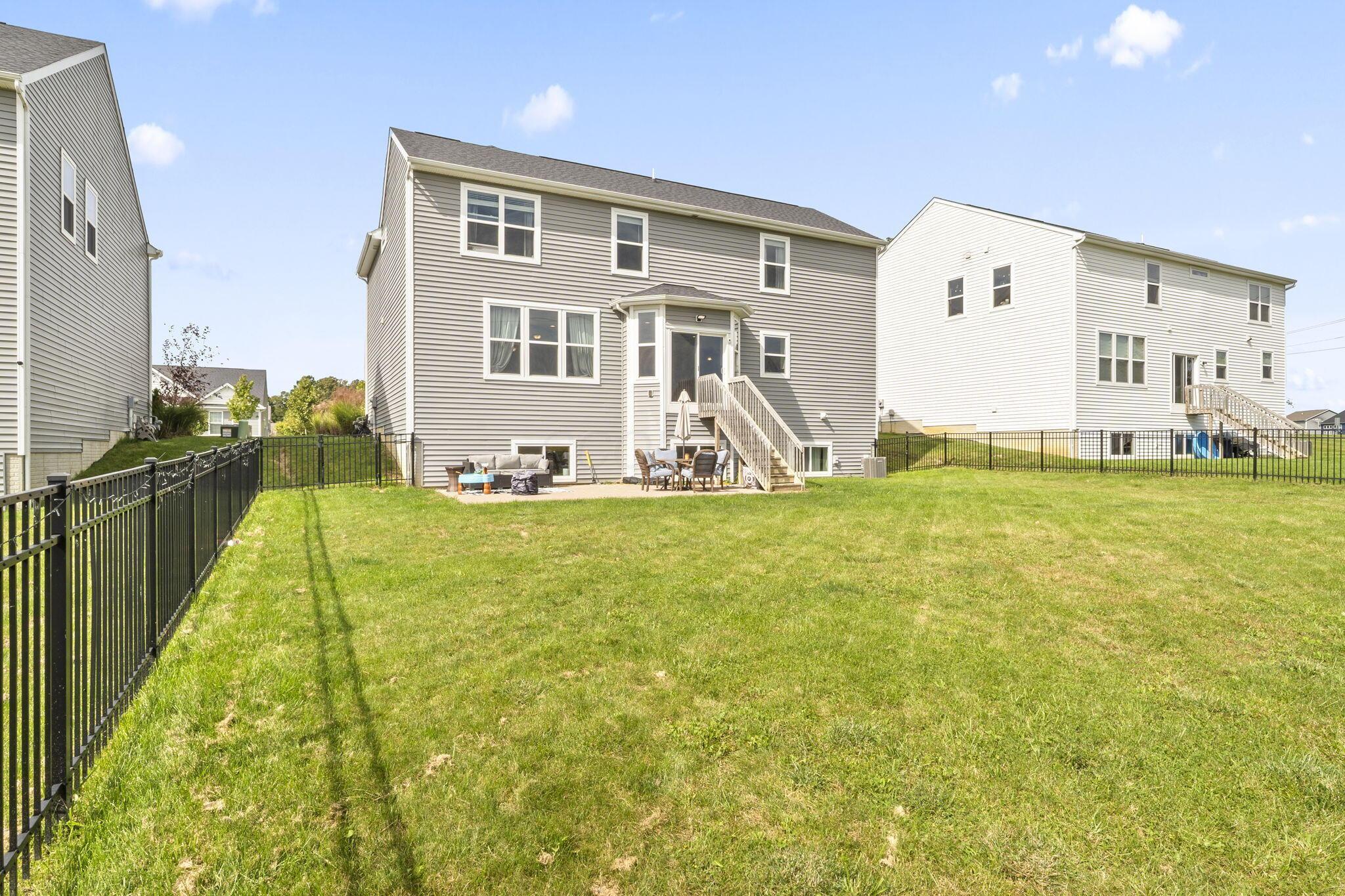 Gray two-story home behind a fenced grassy backyard, with patio seating and rear deck stairs.