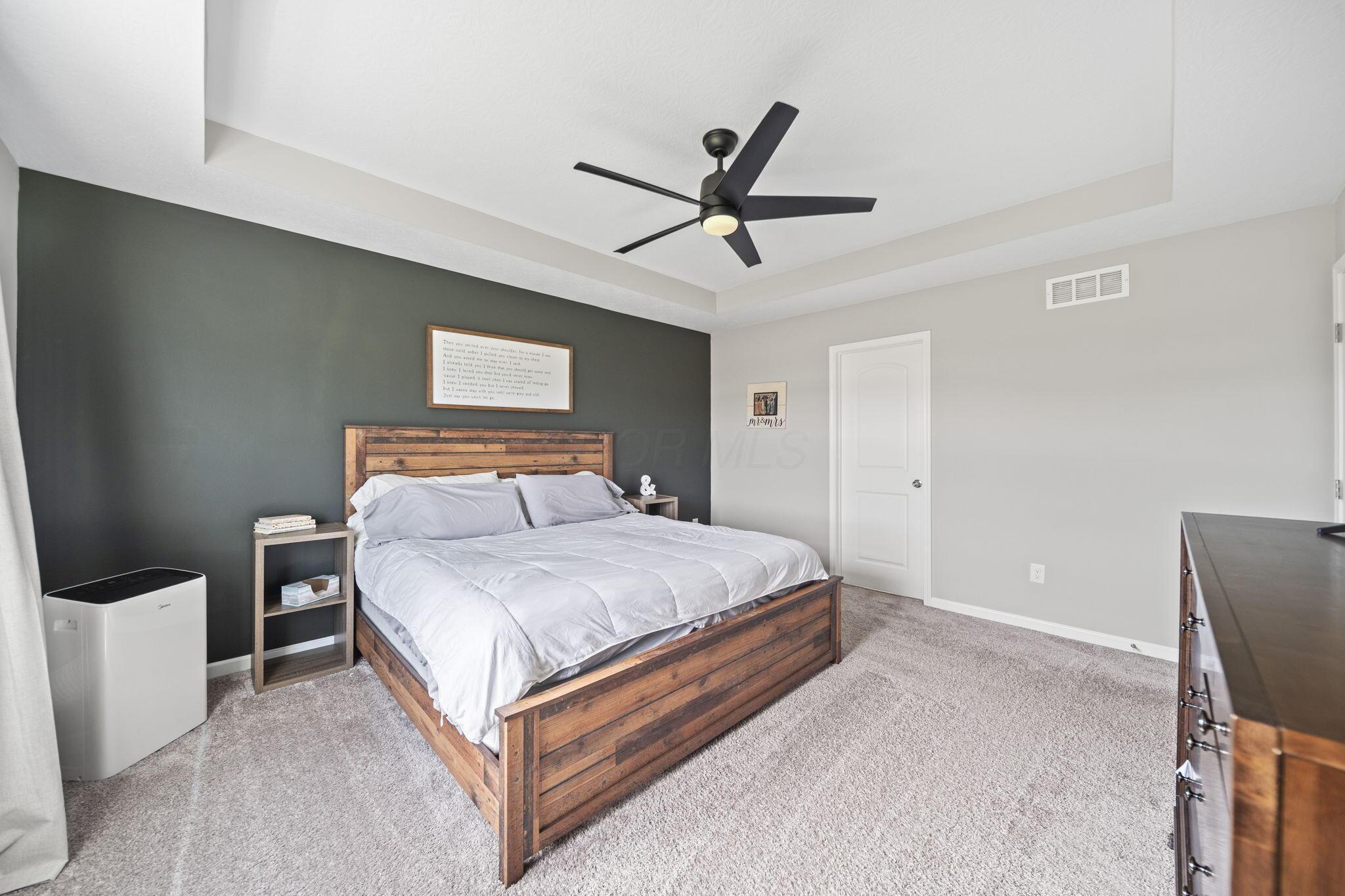 Bedroom with a rustic wooden bed, white bedding, dark accent wall, and black ceiling fan.