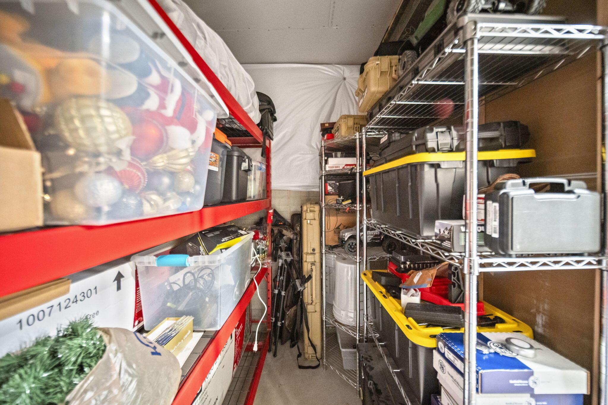 Packed storage room with red shelving, wire racks, plastic bins, and tool cases.