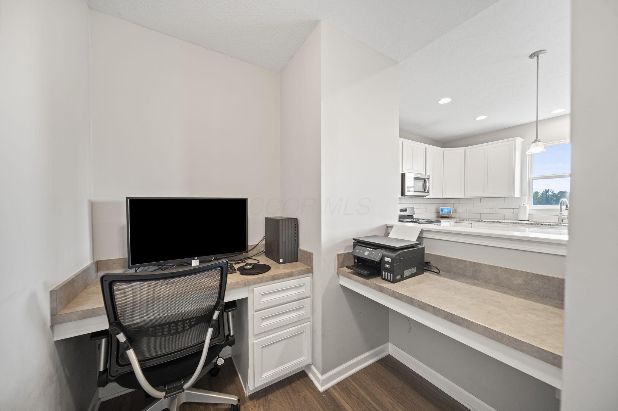 Home office nook with computer and printer beside a bright white kitchen.